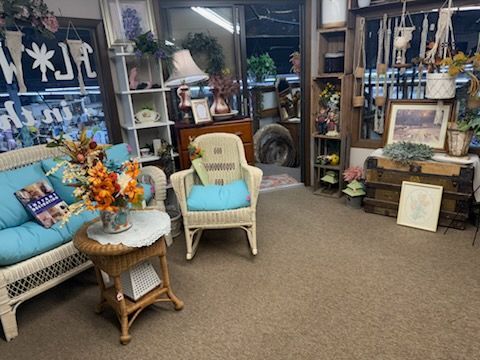 Cozy home decor shop with wicker chairs, floral arrangements, shelves, and framed art displays