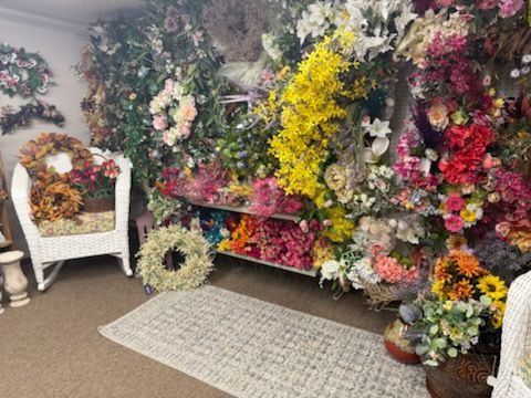 Flower shop display with colorful wreaths, bouquets, and floral arrangements around a rug and chair