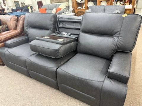 Black leather reclining sofa with center console and cupholders in a furniture showroom