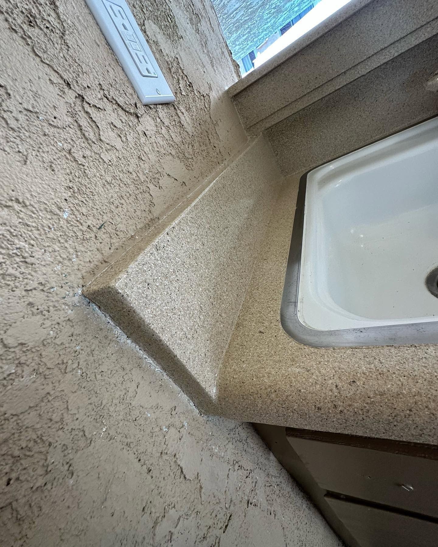 Bathroom sink and countertop with a speckled beige surface near a window.
