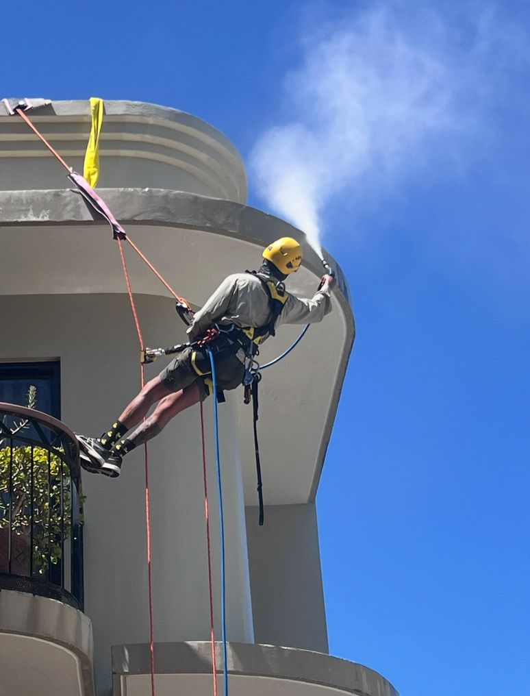 A Man is Spraying Water on the Side of a Building — Dezigner Finishes Professional Painting & Decorating in Palmview, QLD