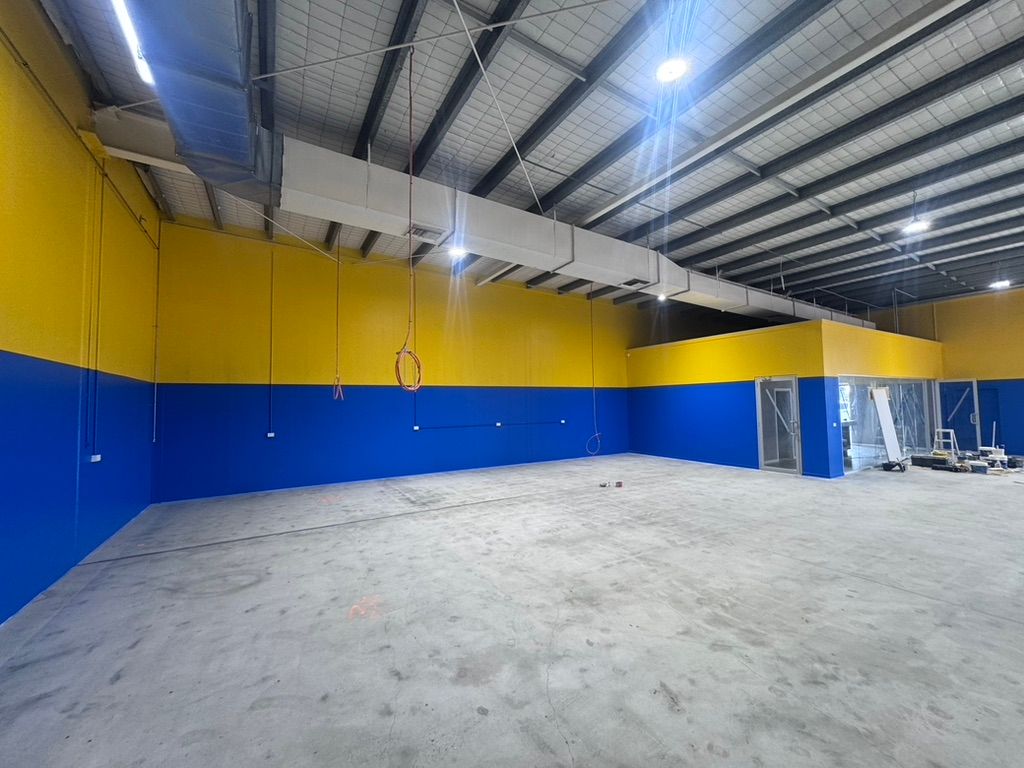 A Man is Painting a Building With a Bucket of Paint — Dezigner Finishes Professional Painting & Decorating in Coolum, QLD