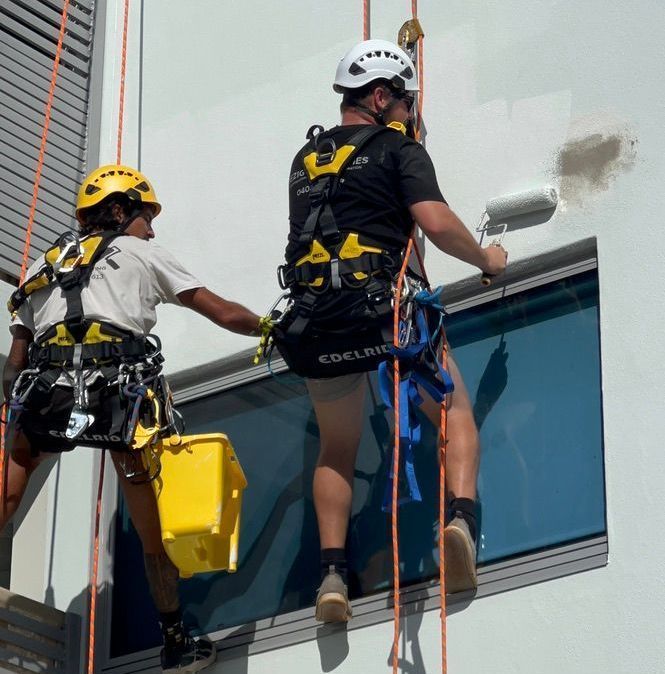 A Man is Painting a Building With a Roller — Dezigner Finishes Professional Painting & Decorating in Coolum, QLD
