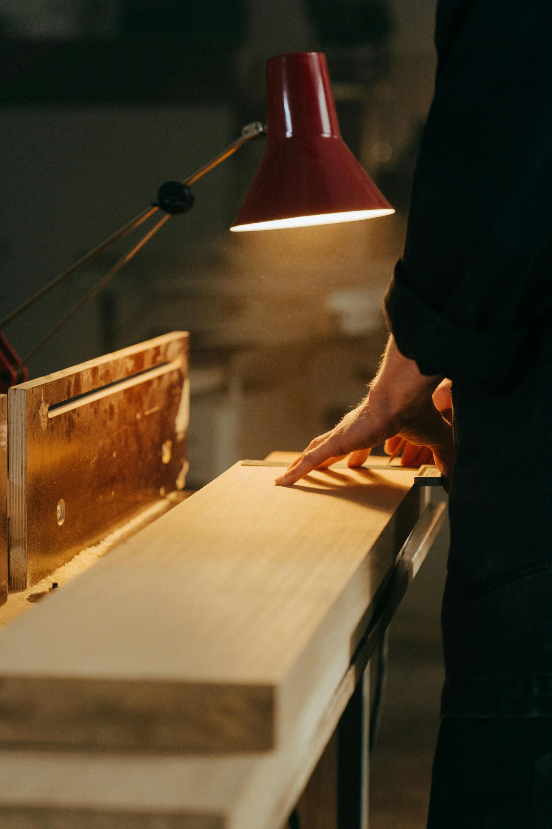 Person using a saw to cut wood under a red desk lamp.