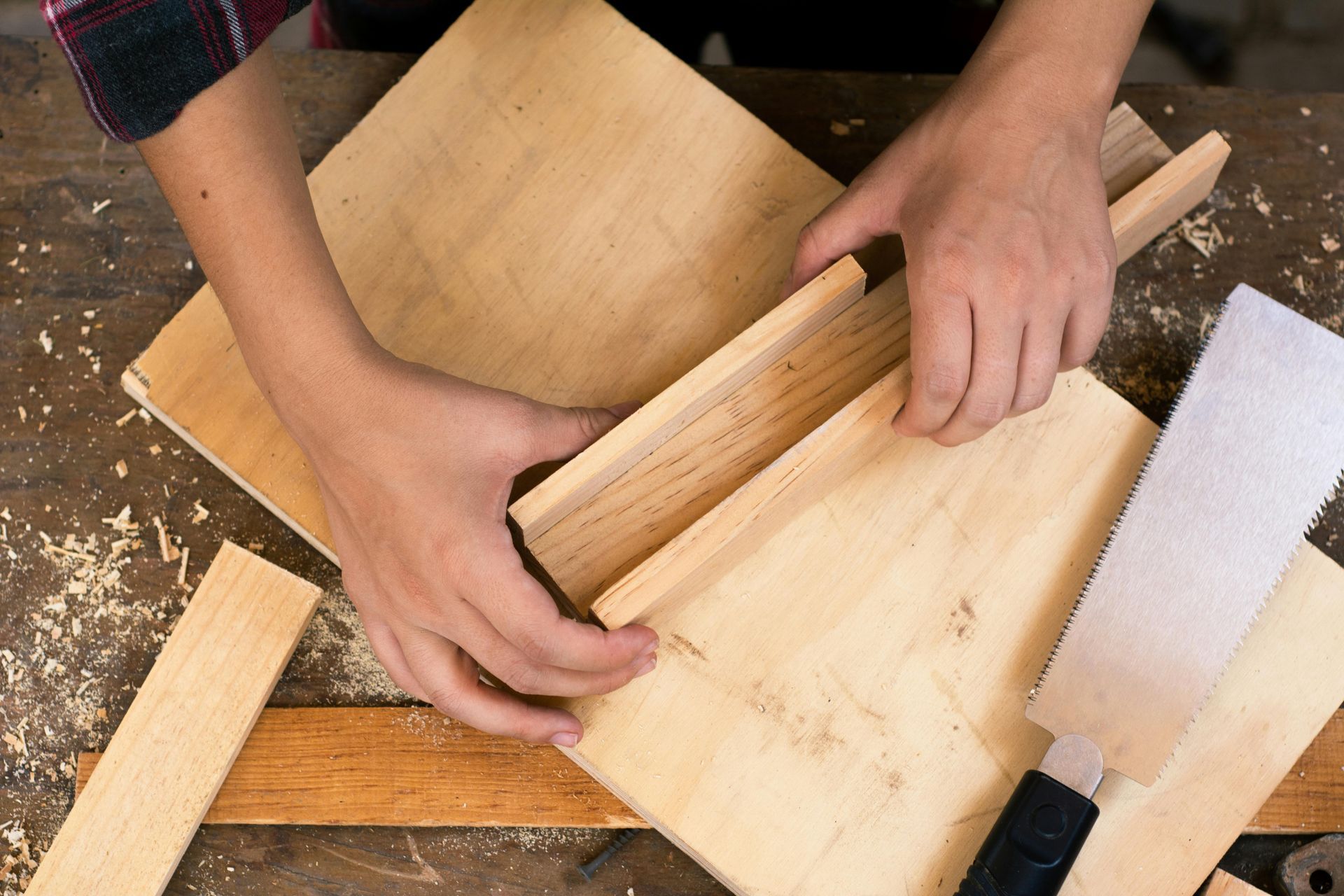 Hands assembling wooden pieces, likely for a woodworking project, with a spatula and scattered sawdust.