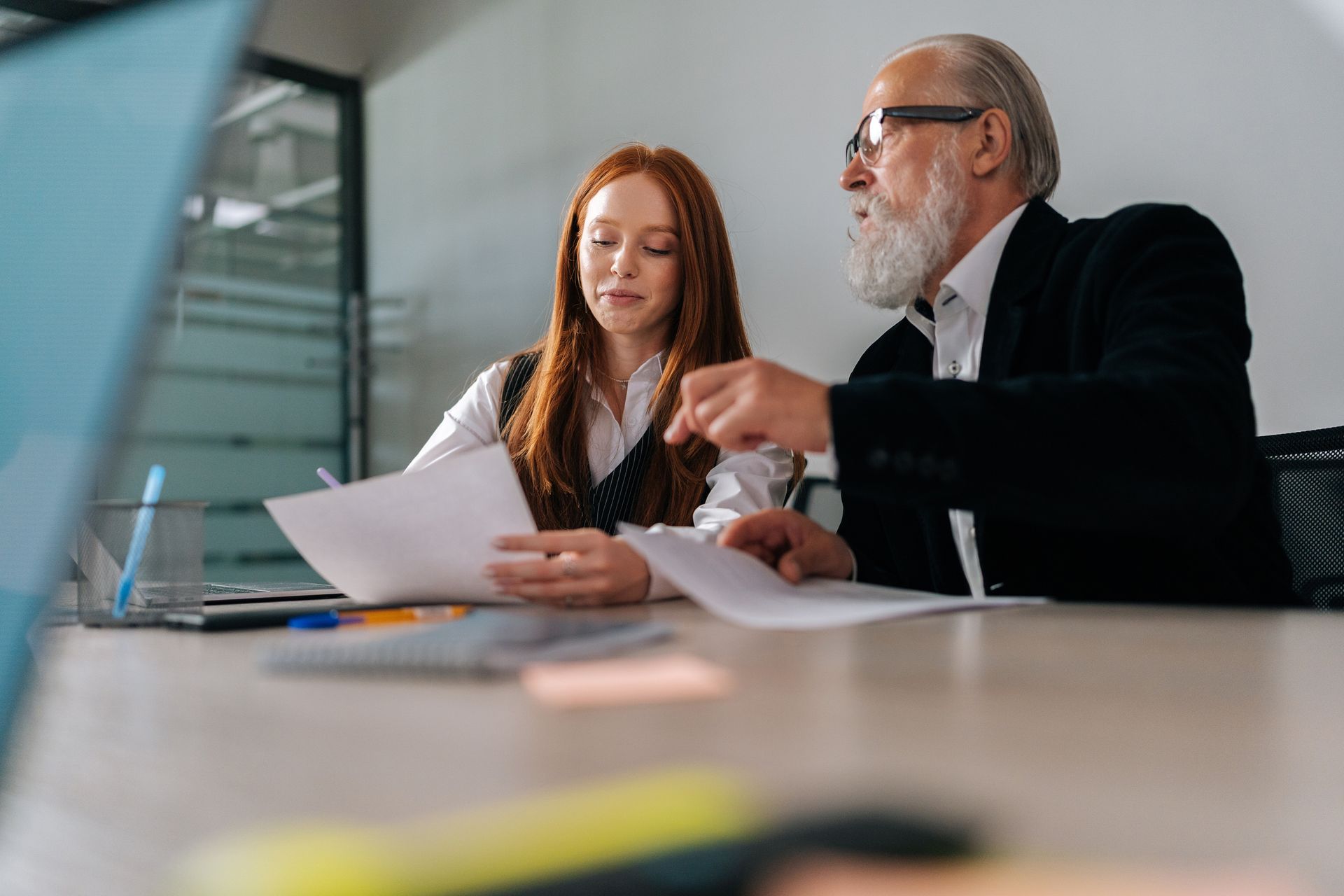 Two colleagues discuss documents at a conference table in a modern office.