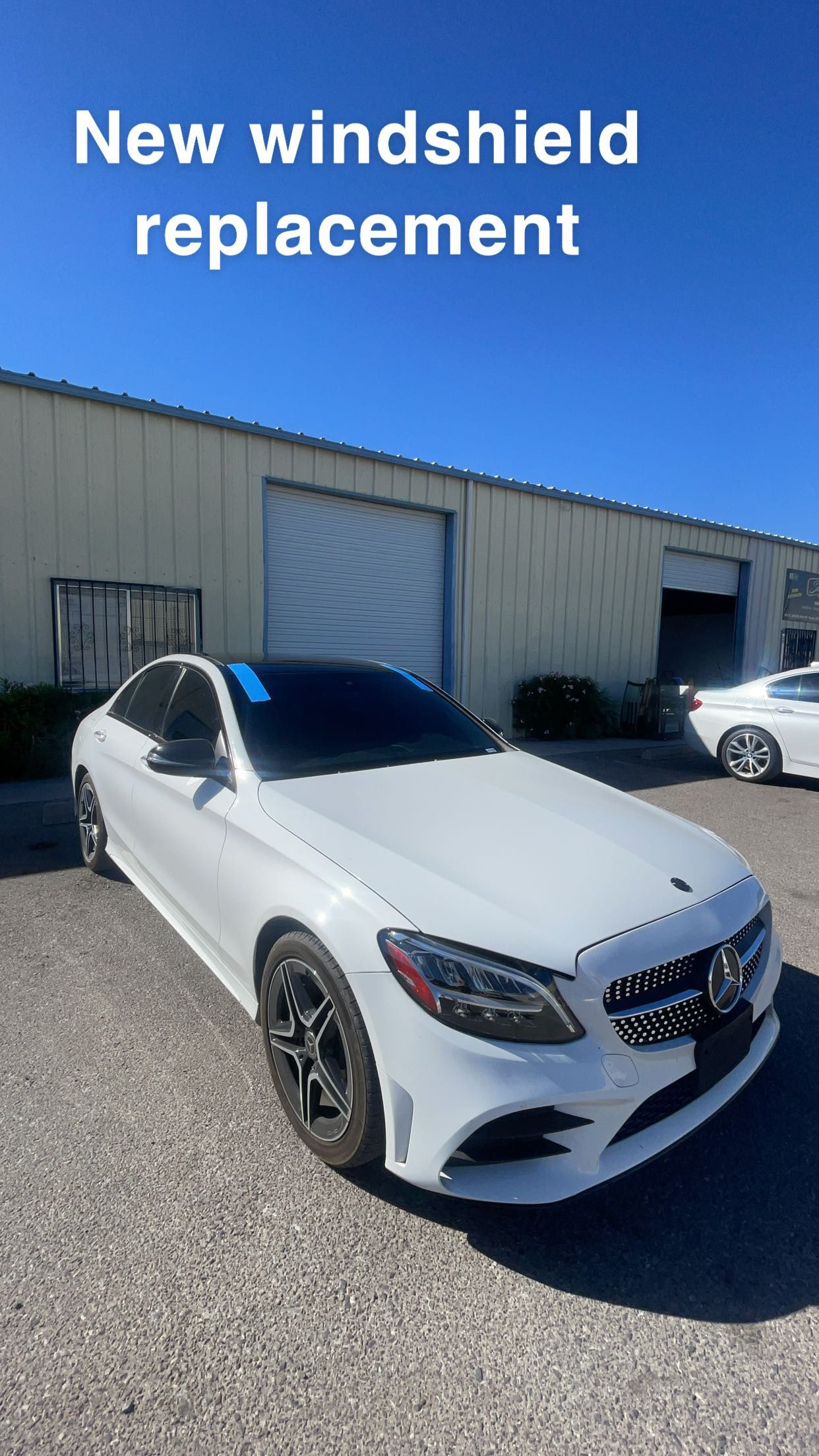 A white car with a new windshield replacement is parked in front of a building.