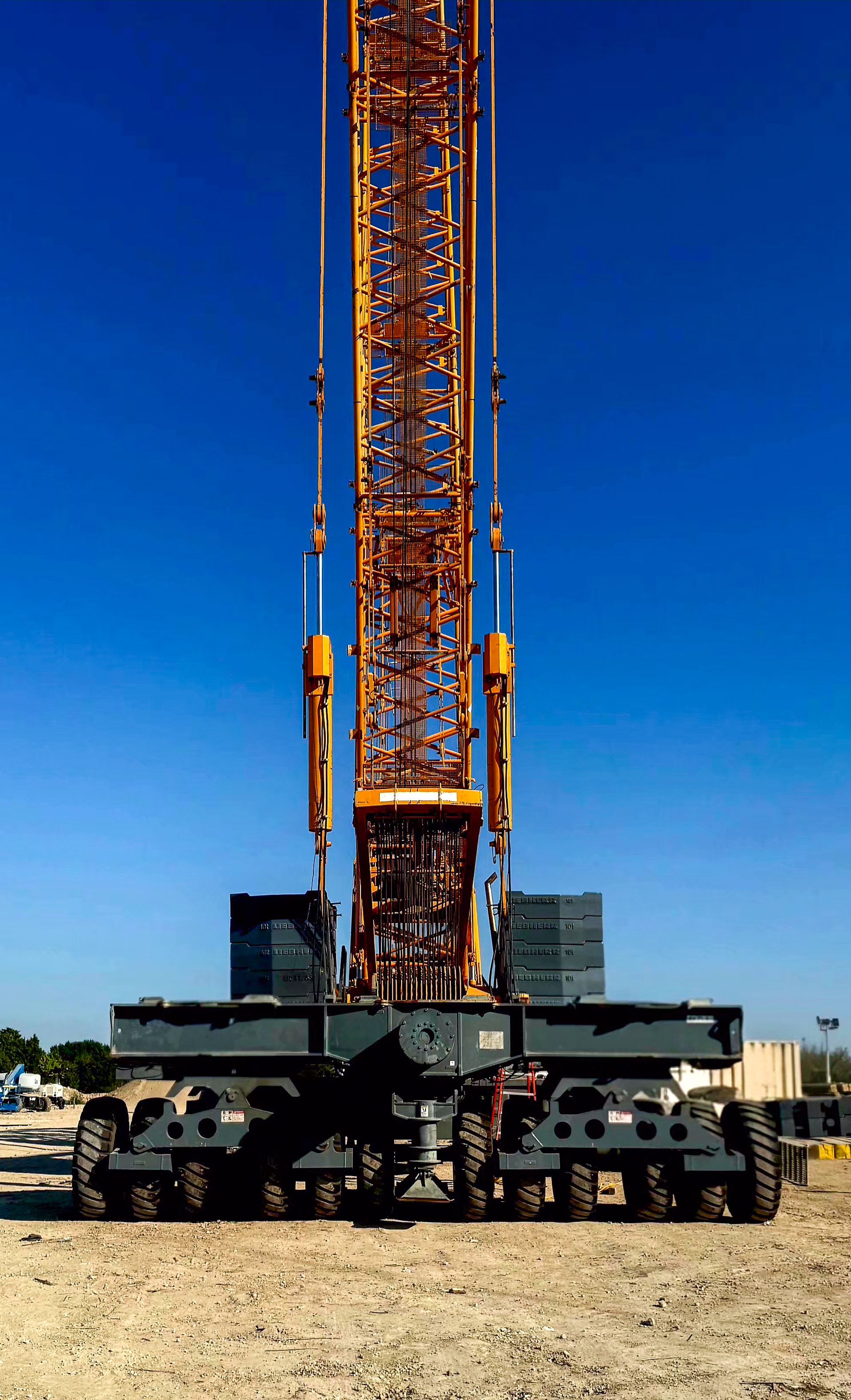 A large yellow construction crane with a long boom against a blue sky, standing on a construction site.
