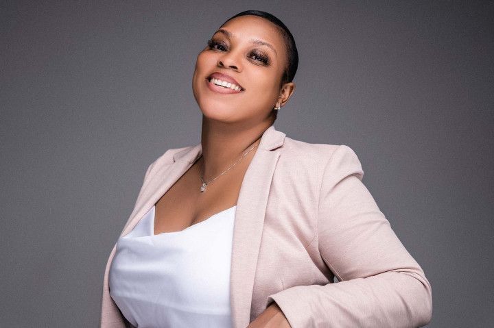 Smiling woman in a light pink blazer over a white top against a gray background
