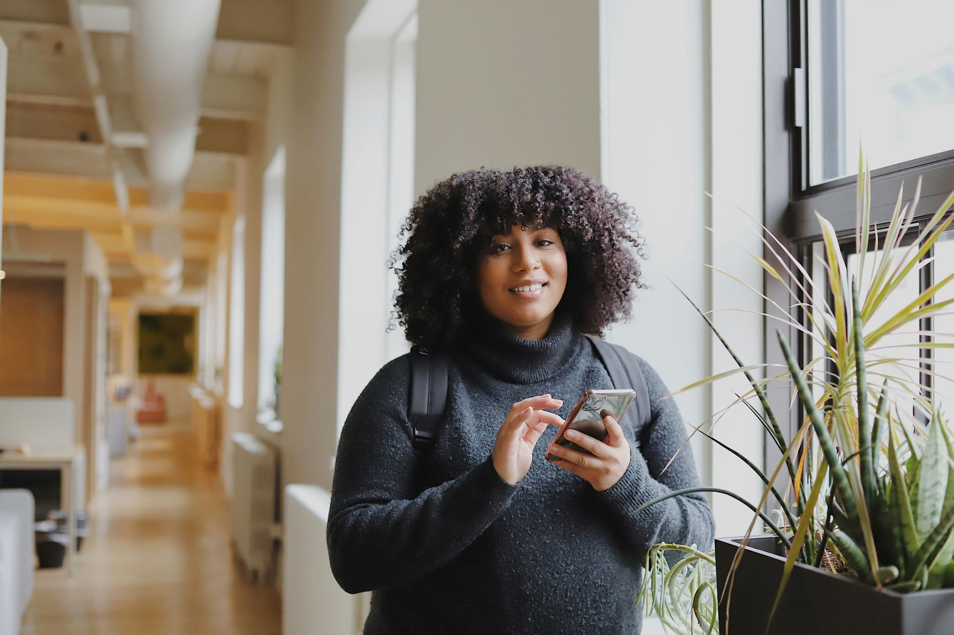 A woman is standing in a hallway looking at her cell phone.