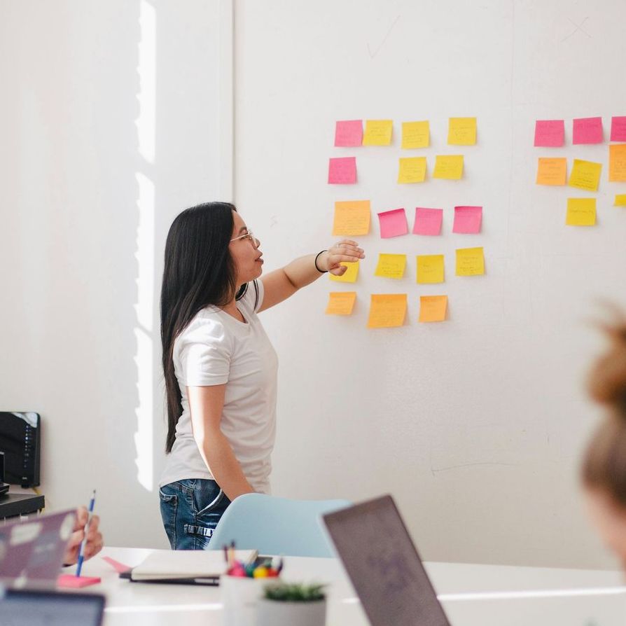 A woman is pointing at sticky notes on a wall.