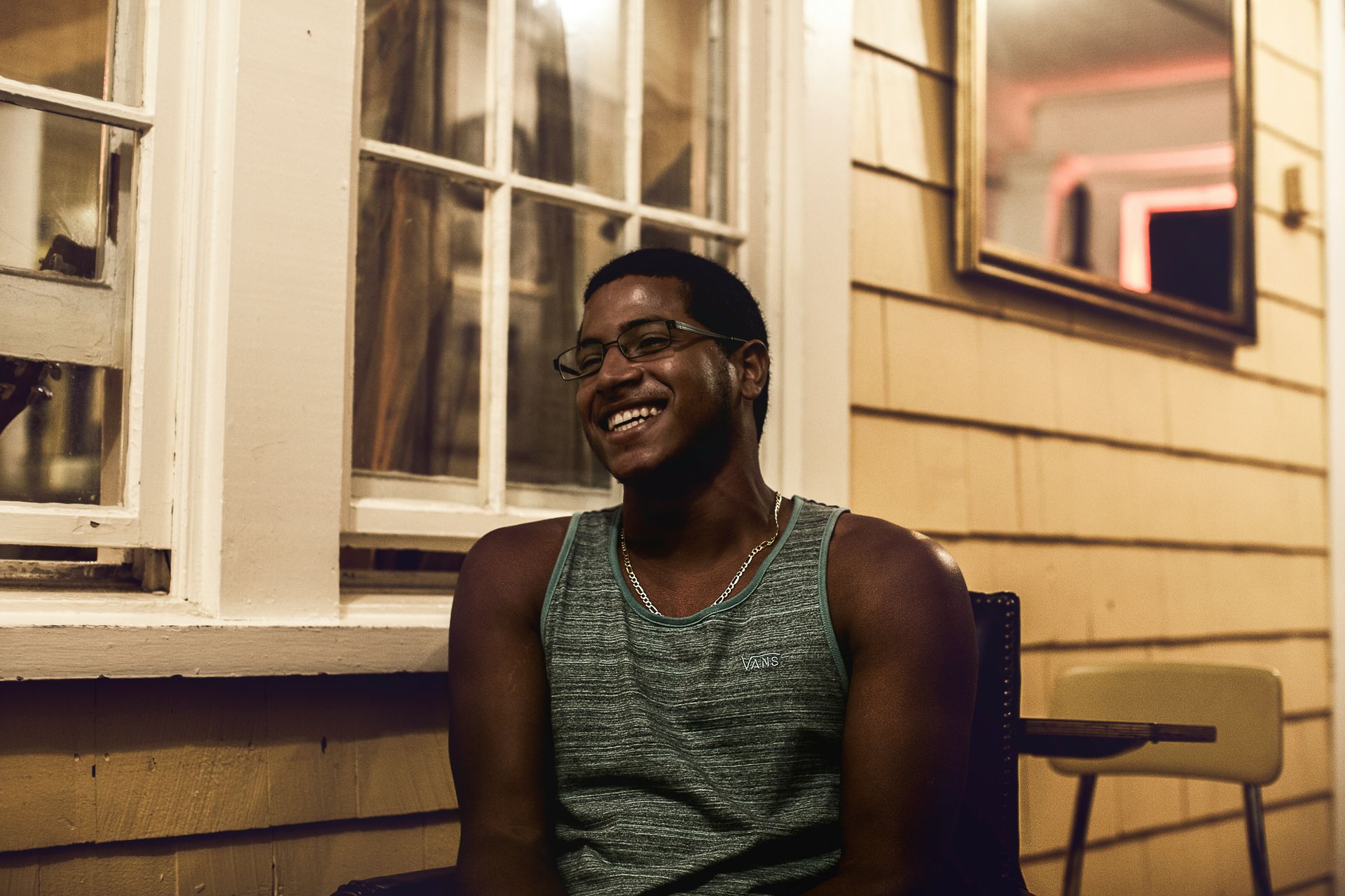 A man wearing glasses and a tank top is sitting in front of a window.