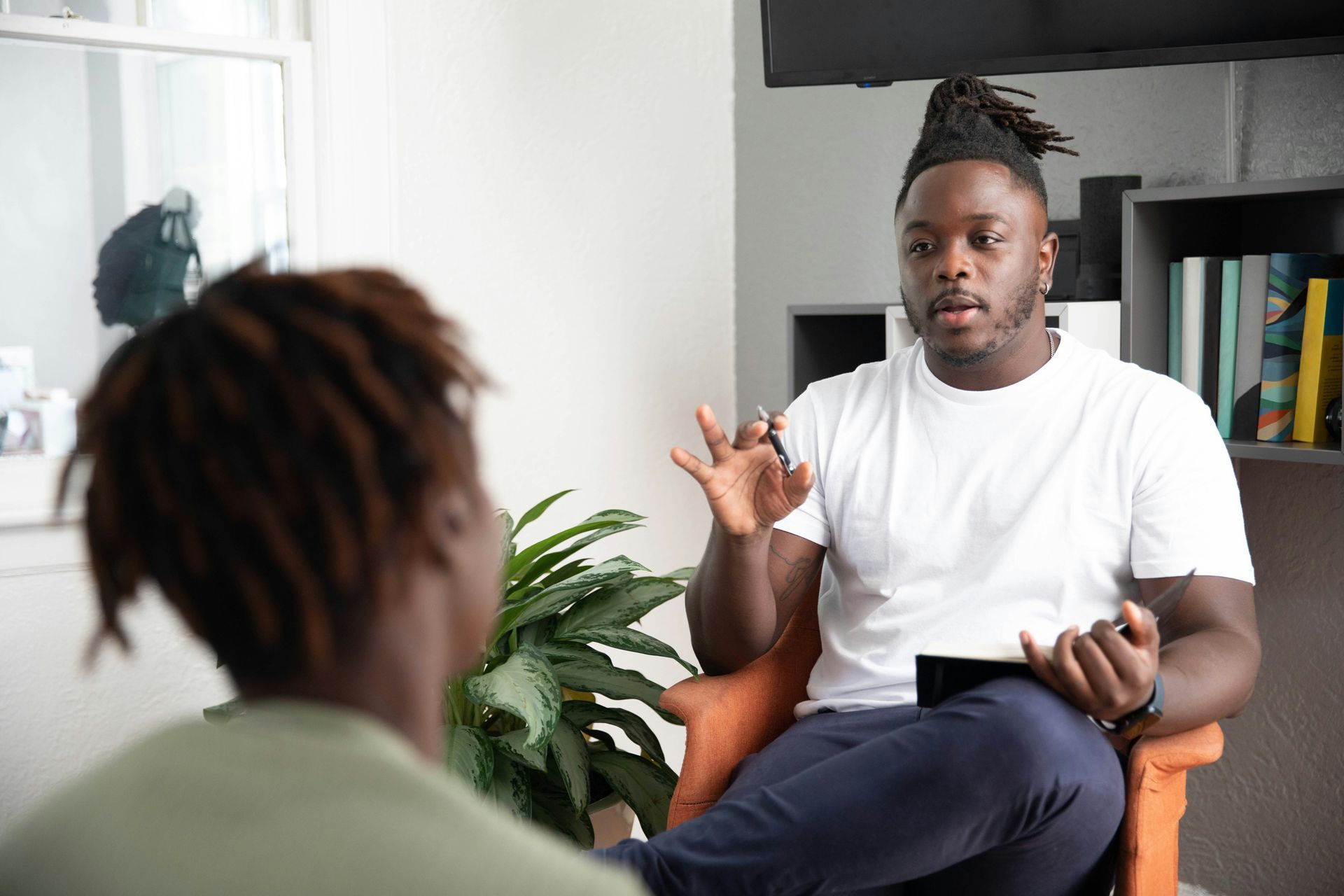 A man is sitting in a chair talking to another man.