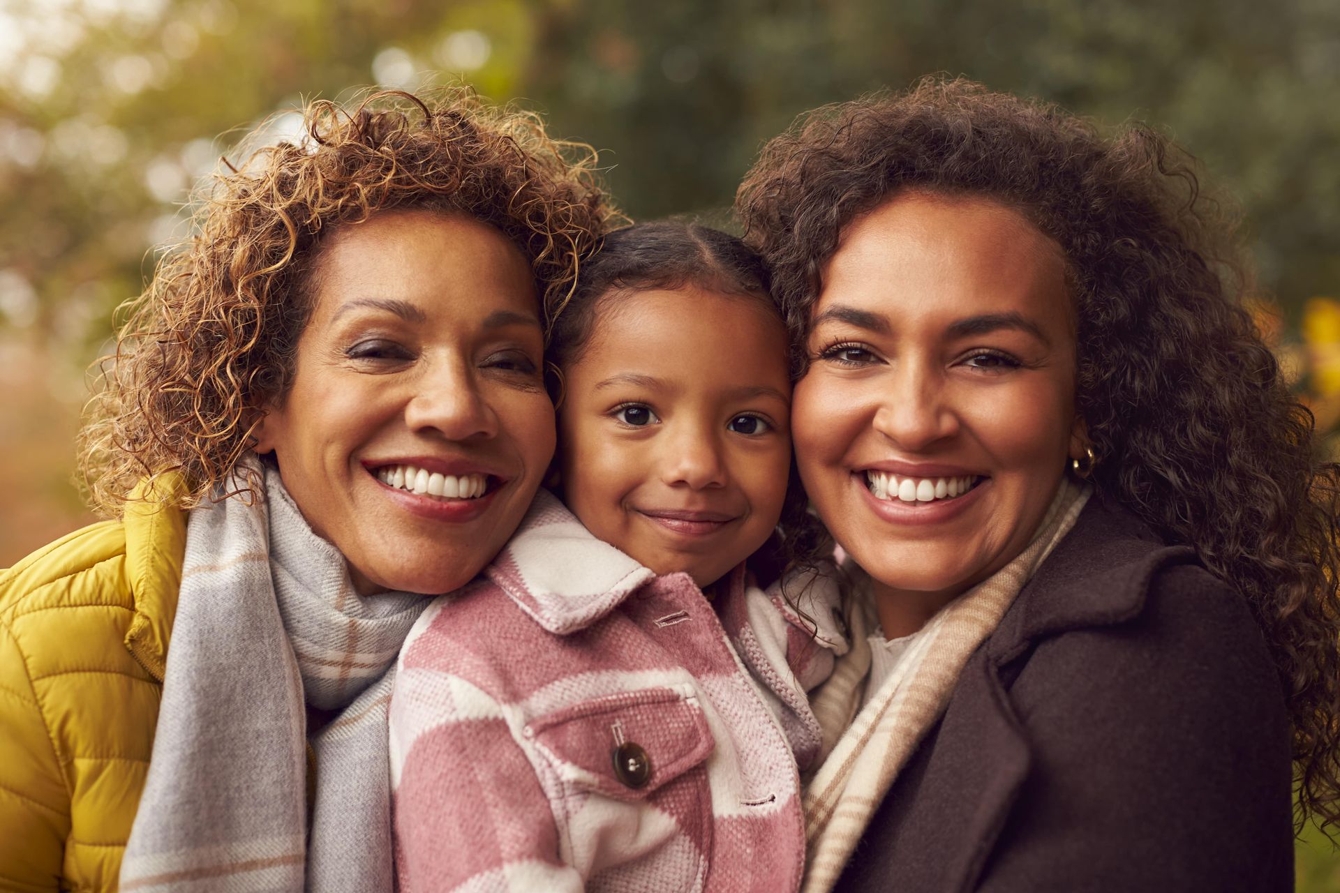 Three women are posing for a picture with a little girl in a park.