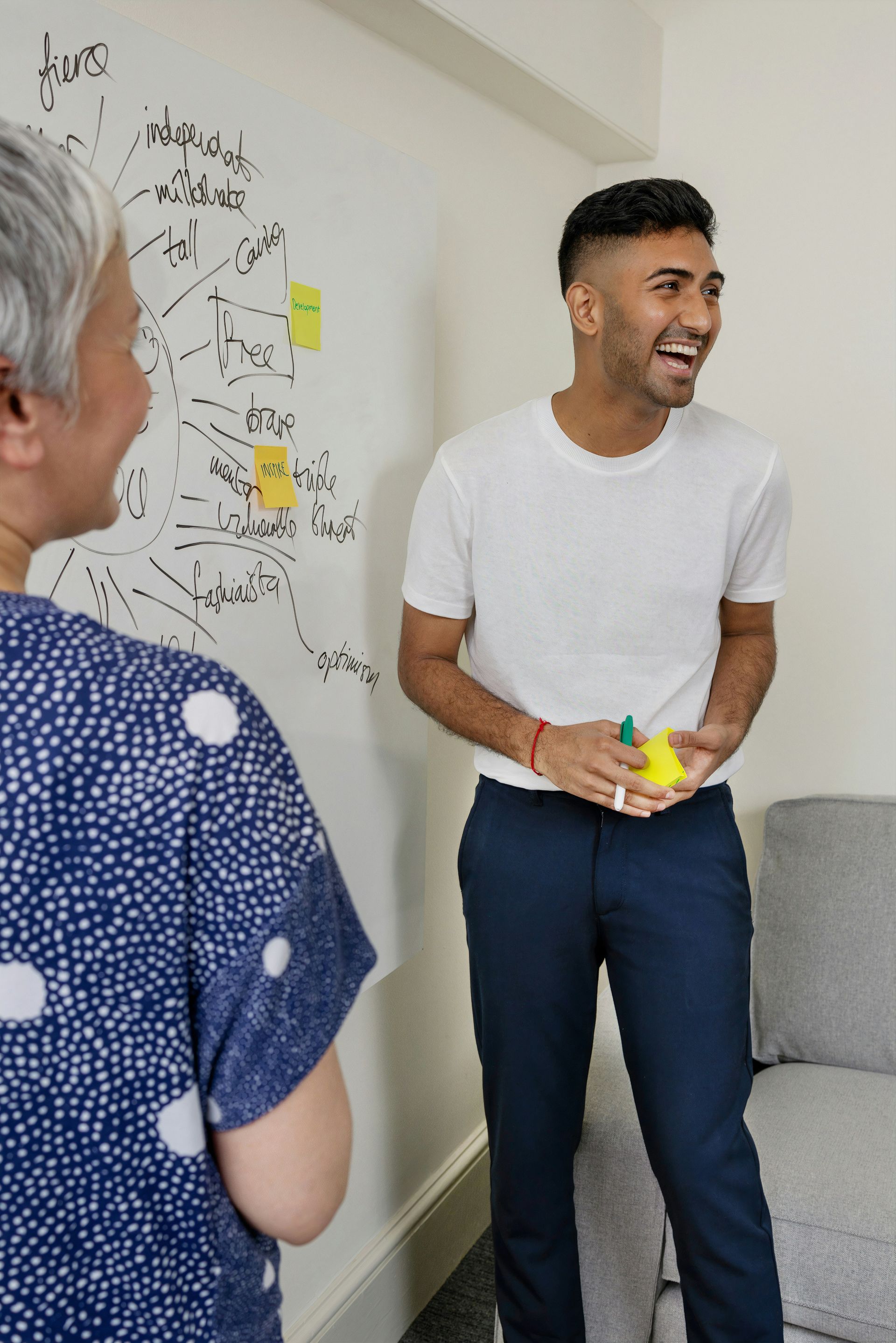 A man and a woman are laughing in front of a whiteboard.