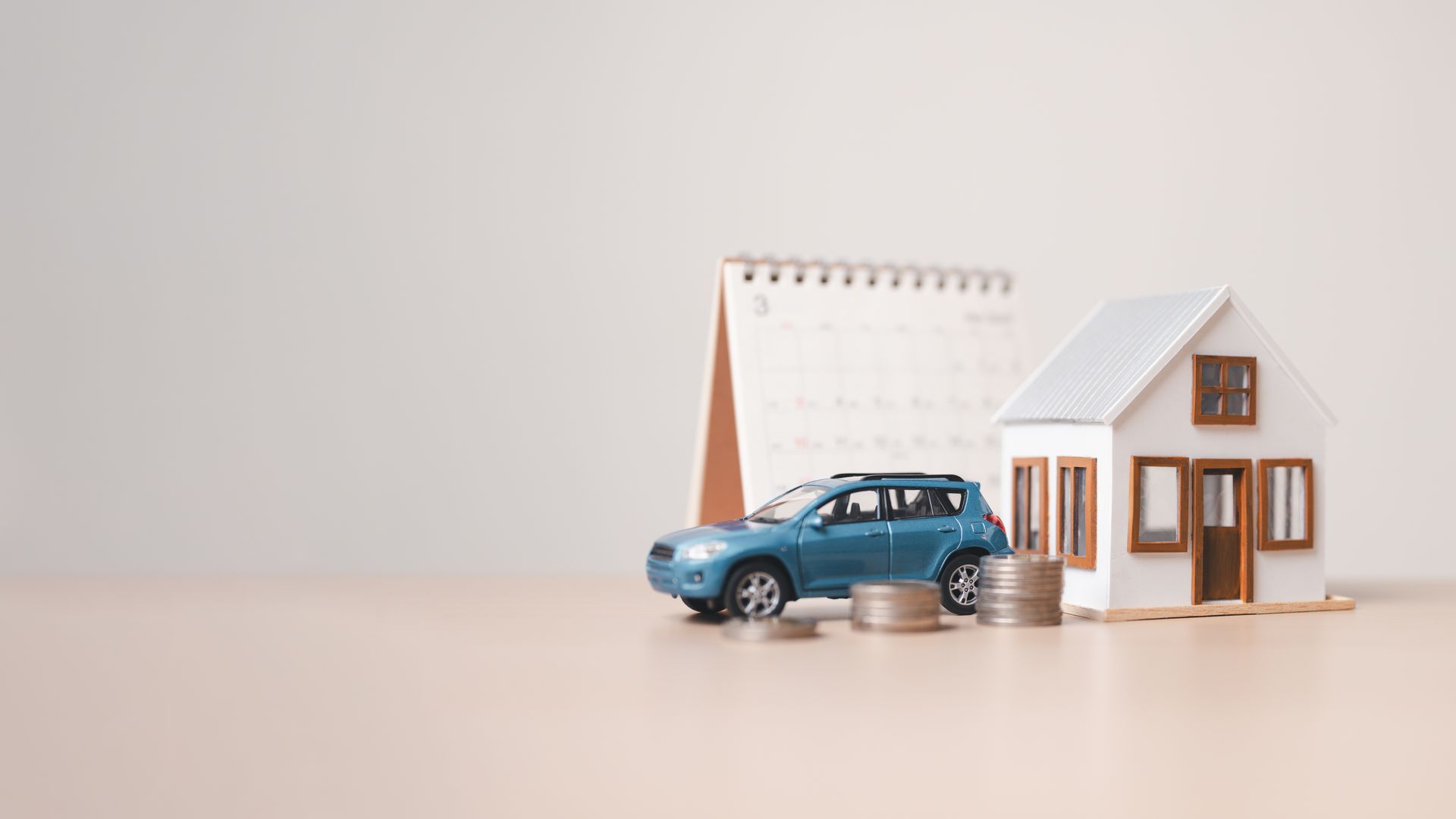 Blue toy car beside a small white house and notebook on a beige surface
