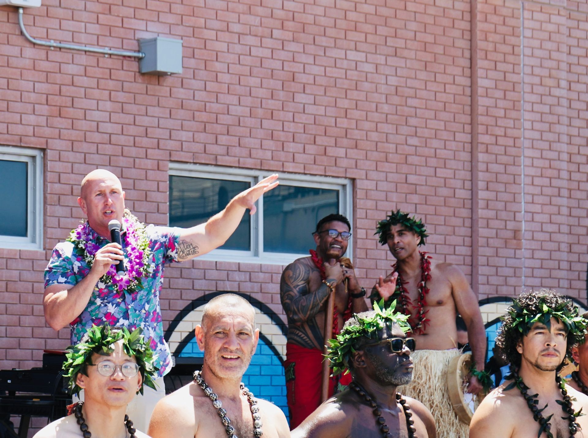 Group of people outdoors by a brick wall, wearing colorful floral leis and posing in a festive scene