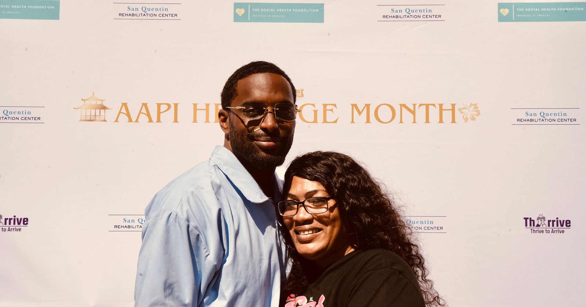 Two people smiling in front of an AAPI Heritage Month backdrop at an event.