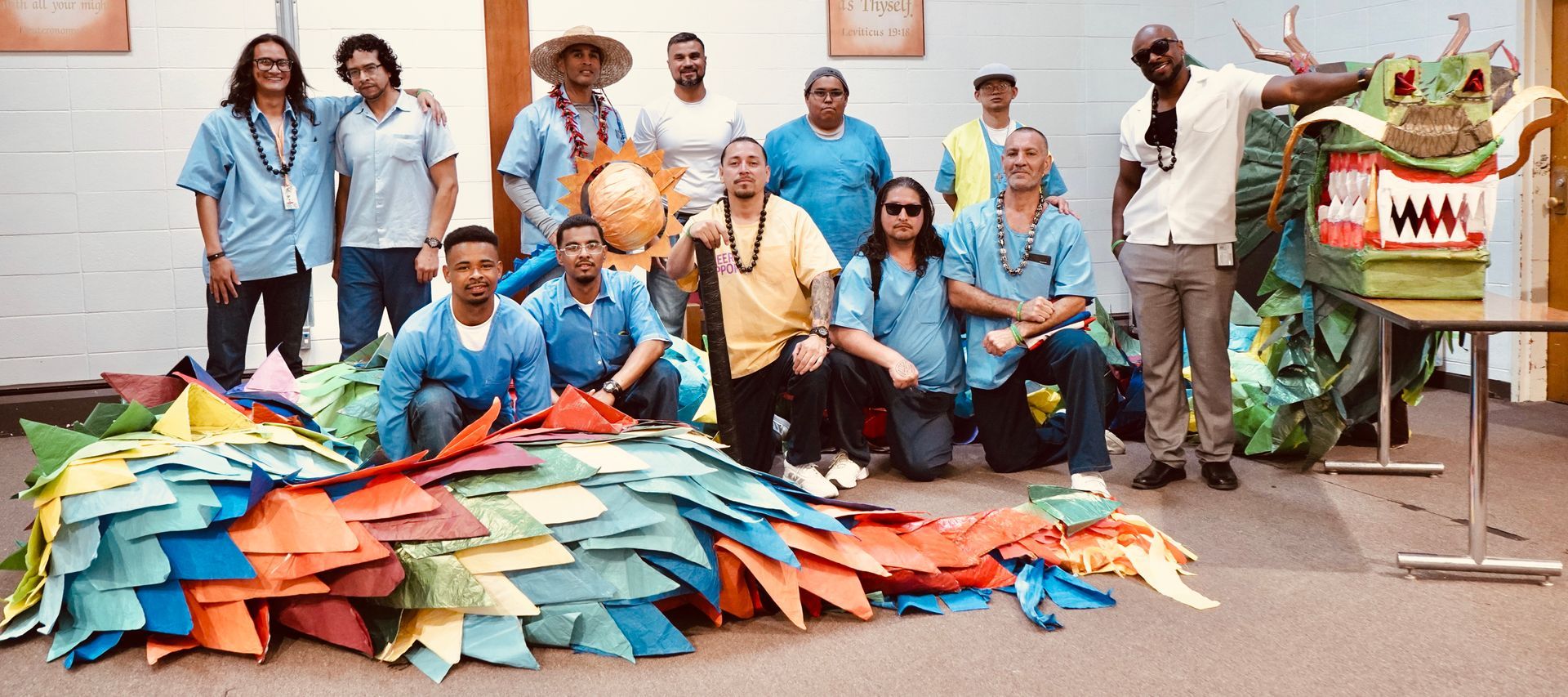 People in blue shirts stand behind a large pile of colorful folded paper on a street, with a decorated cart nearby.