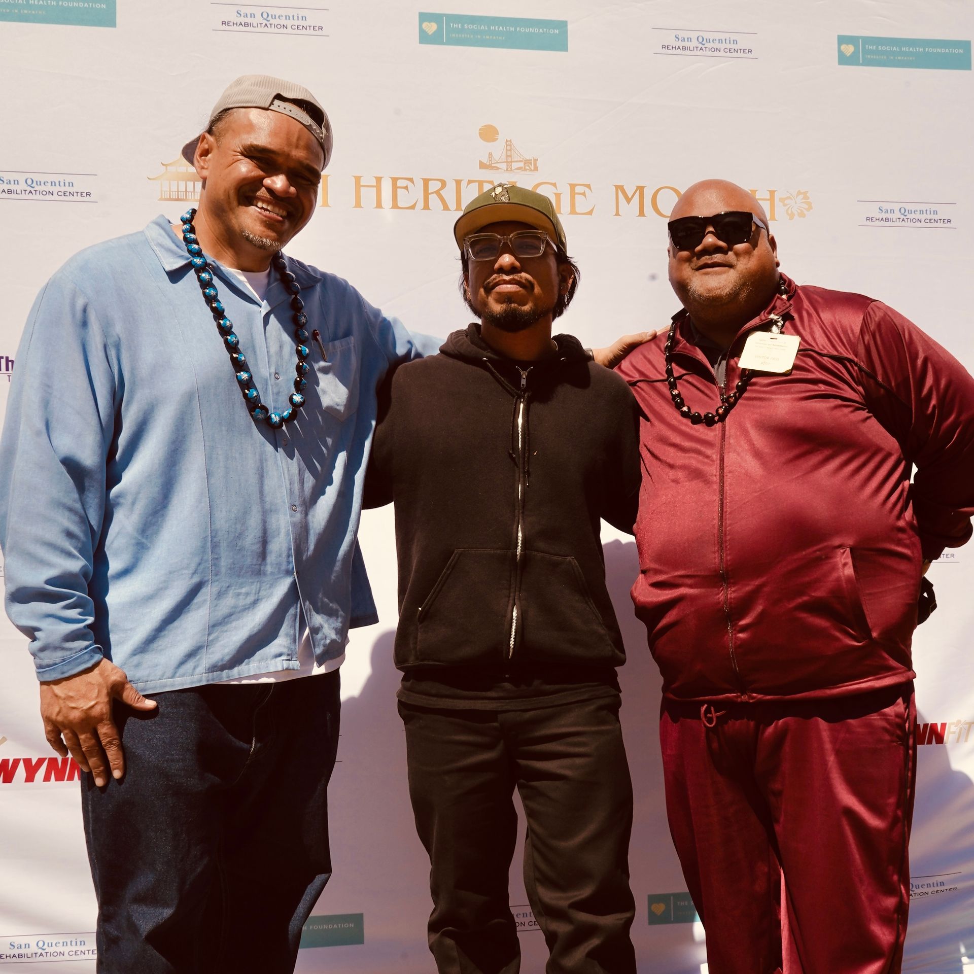 Three people posing together at an outdoor event in front of a branded backdrop.