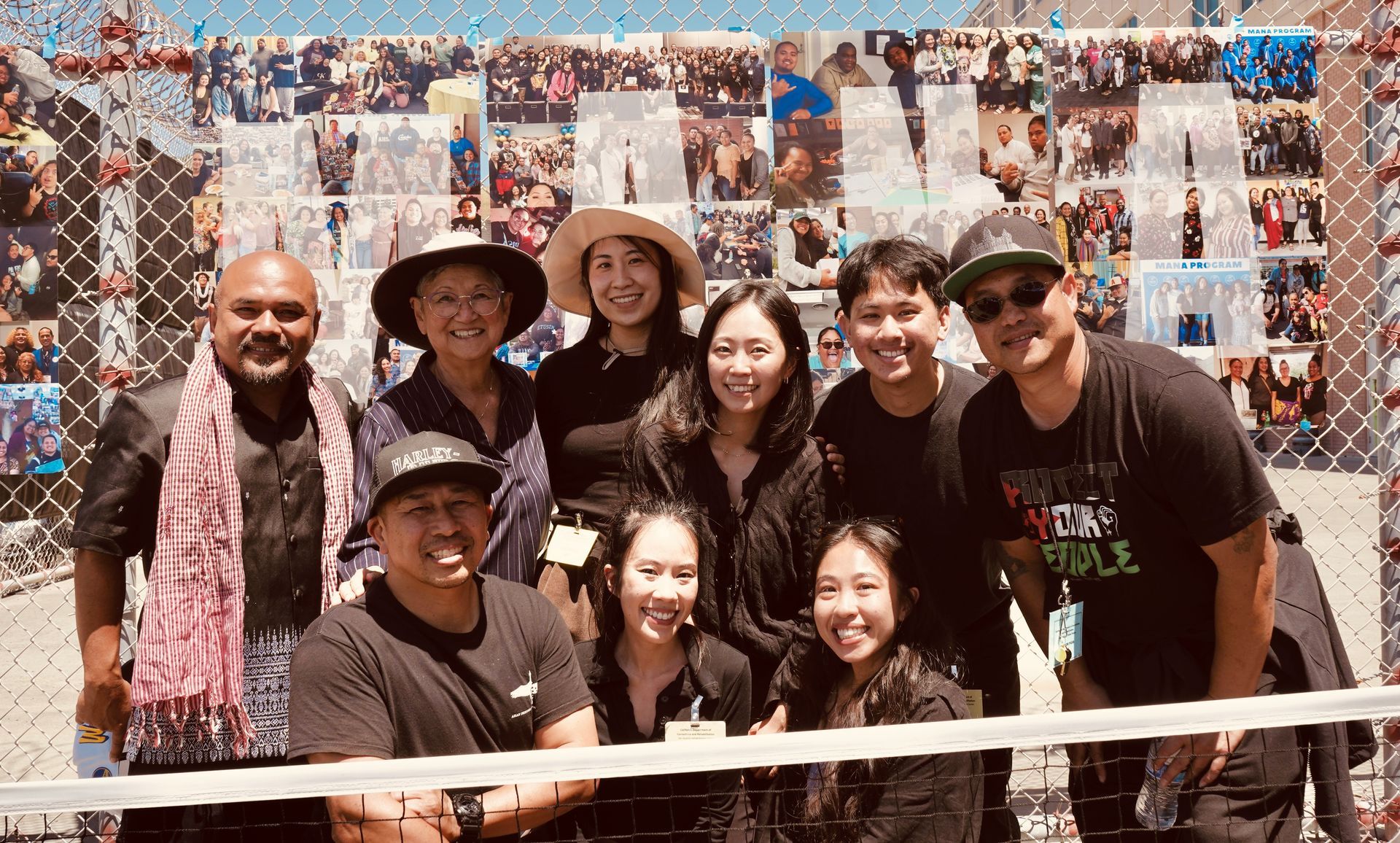 Group of friends smiling in front of a colorful water wall, some wearing hats and sunglasses.