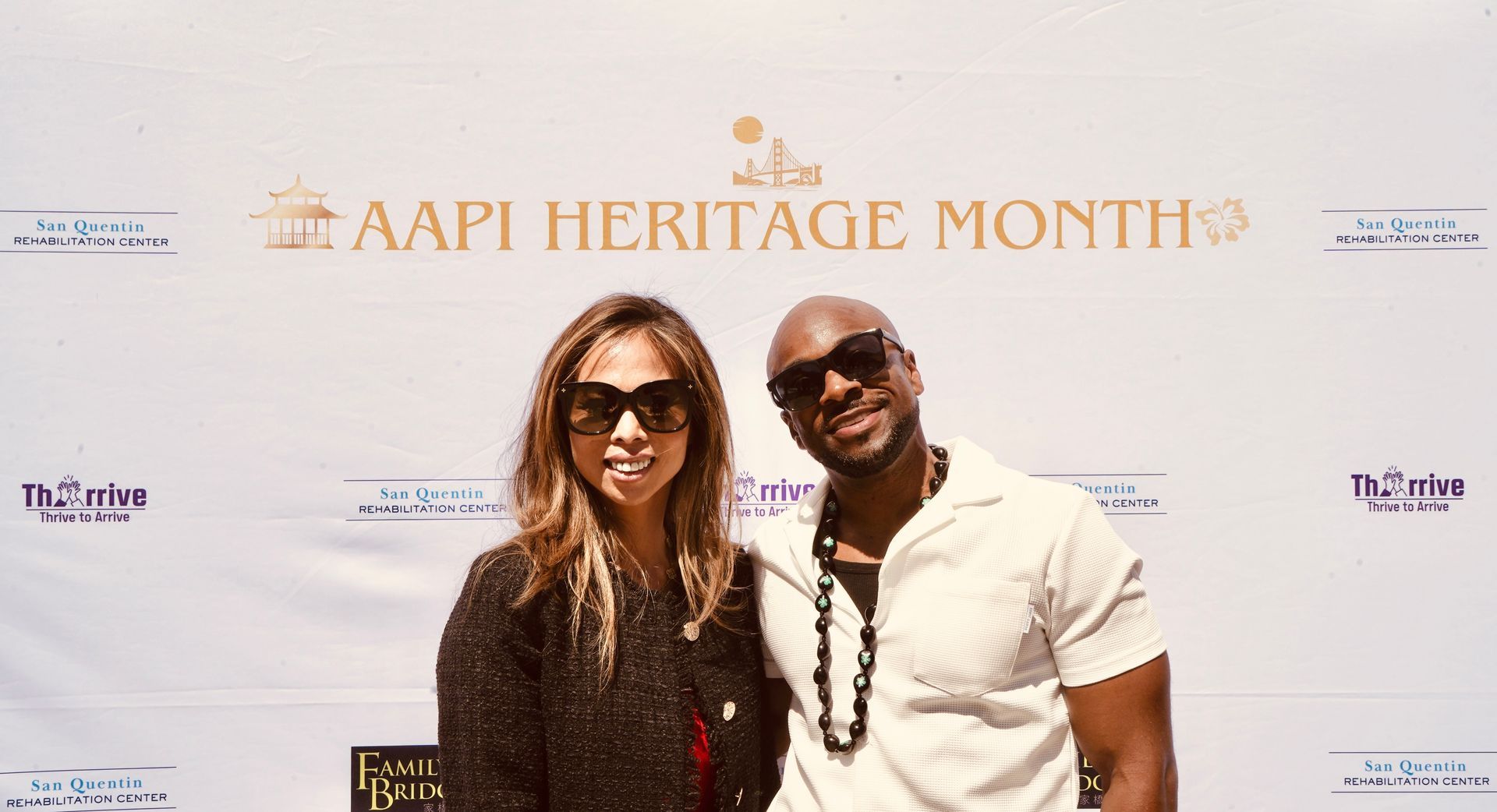 Two people smiling at AAPI Heritage Month event backdrop, standing close together.