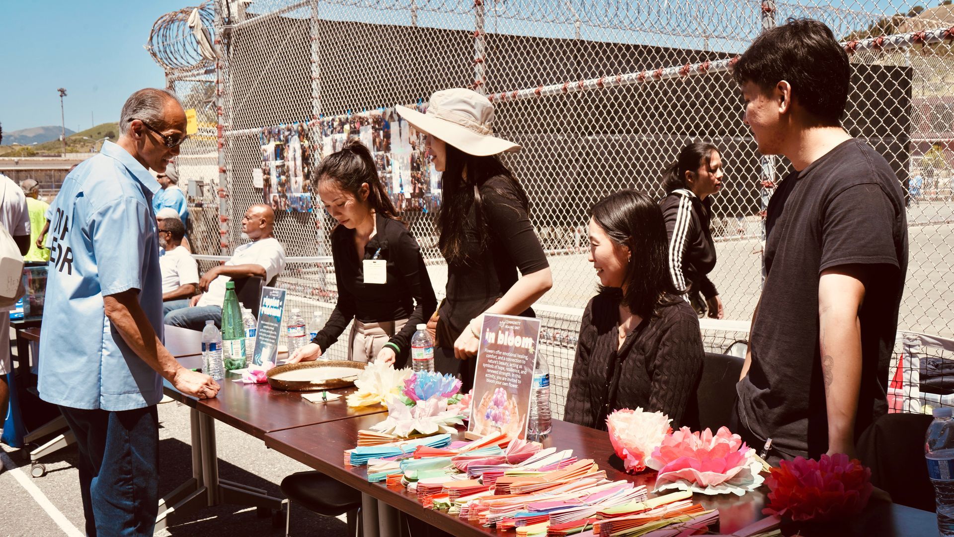 People at an outdoor table selling colorful items under bright sunlight