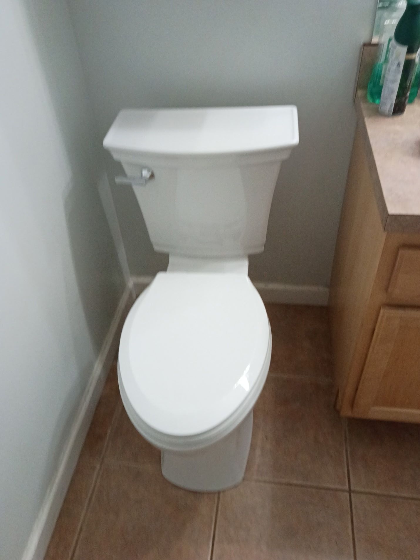 White toilet next to a wooden vanity in a small tiled bathroom corner