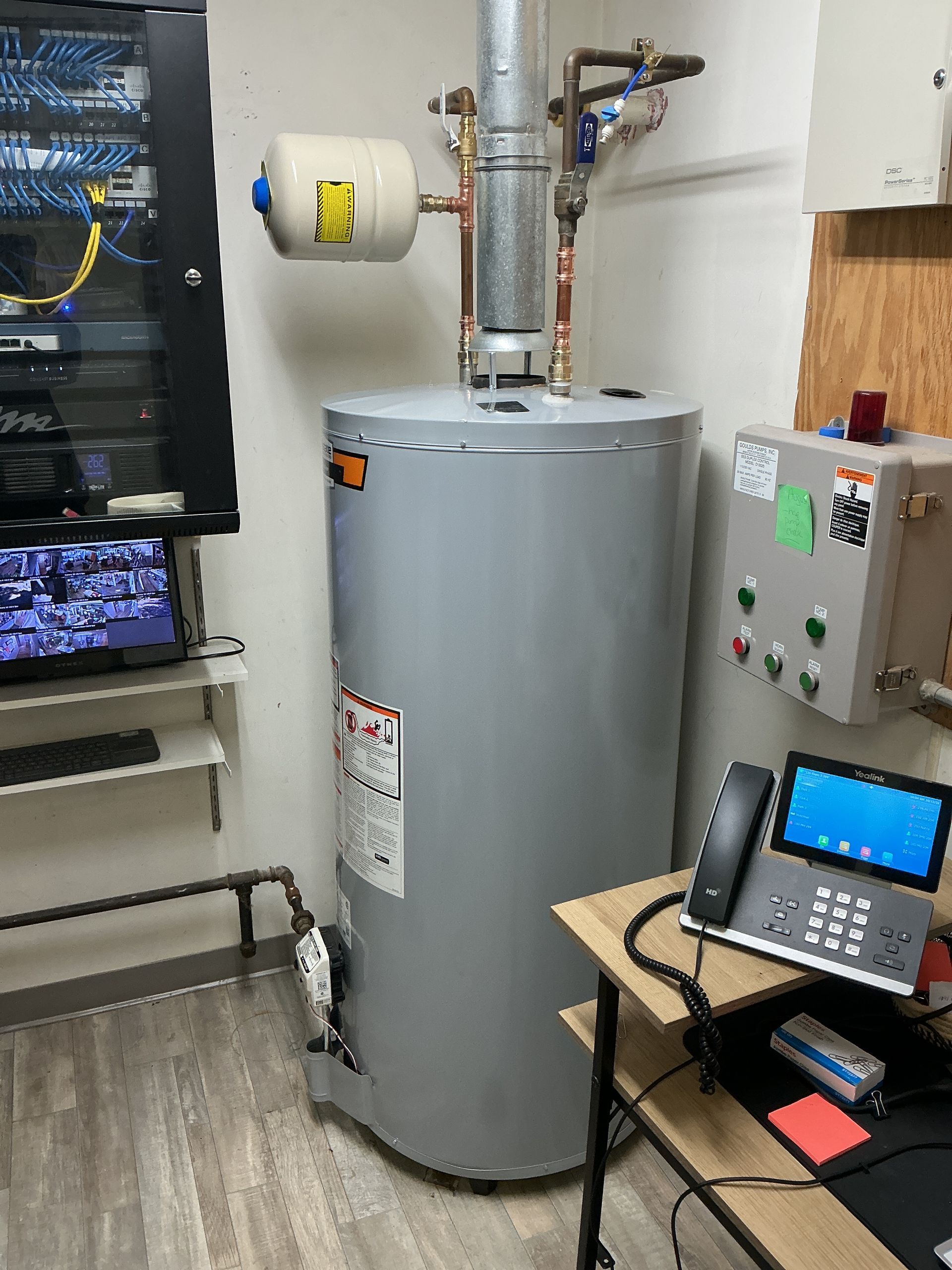 Gray water heater in a utility room, with wall-mounted controls and a small phone on a table.