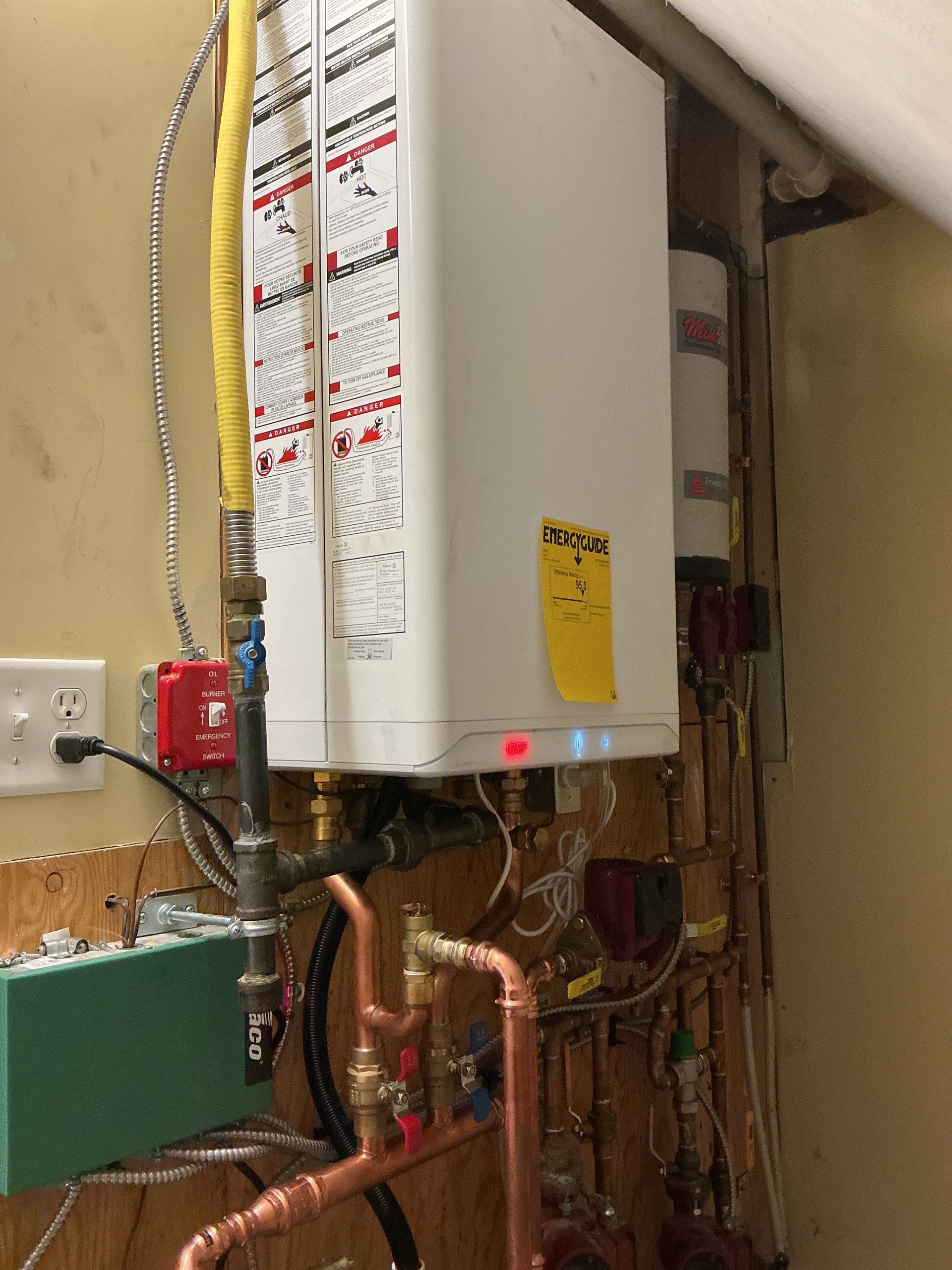 Wall-mounted water heater with copper pipes and yellow gas line in a utility area