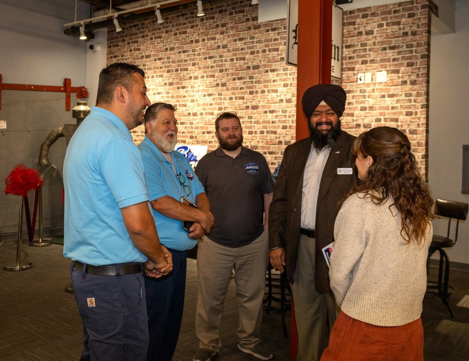 Five people chatting in an industrial-style room with exposed brick walls and pipes.