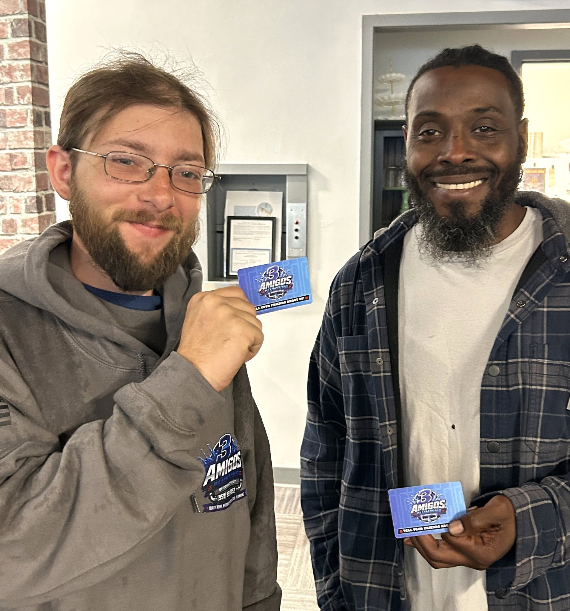 Two smiling men indoors holding blue cards in a hallway