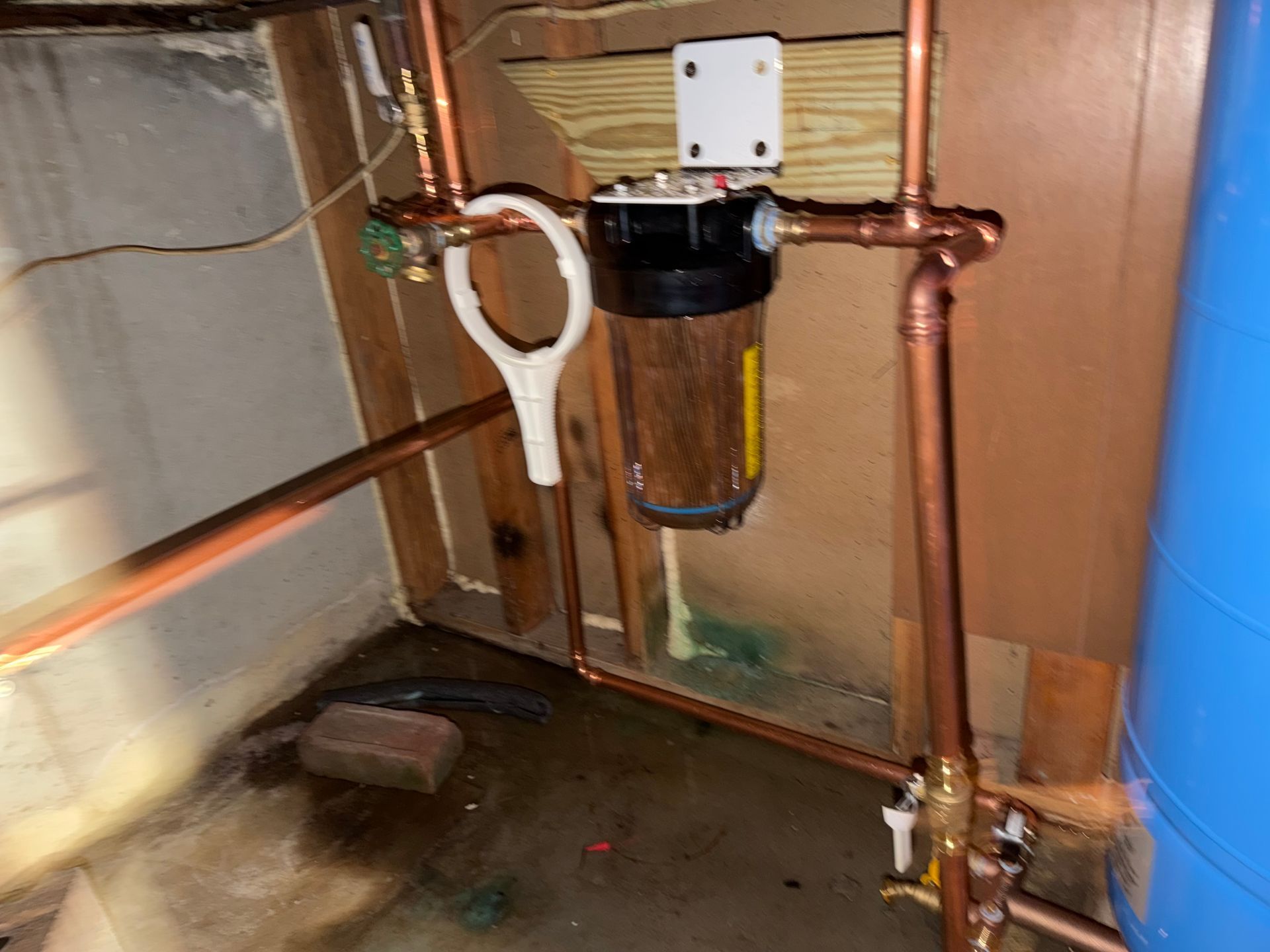 Under-sink plumbing with copper pipes, shutoff valve, and water filter in a cabinet