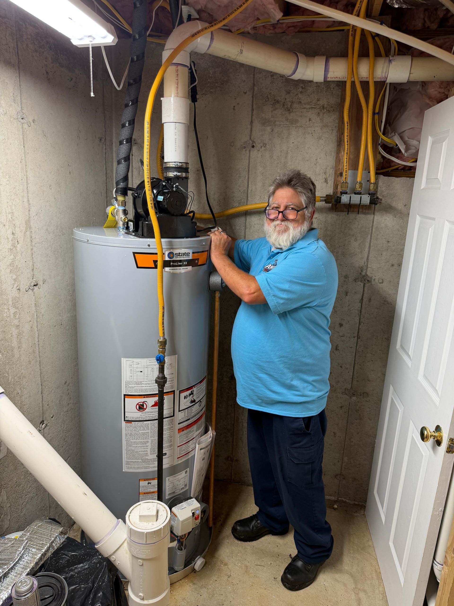Man in blue shirt adjusting plumbing beside water heater in a utility room