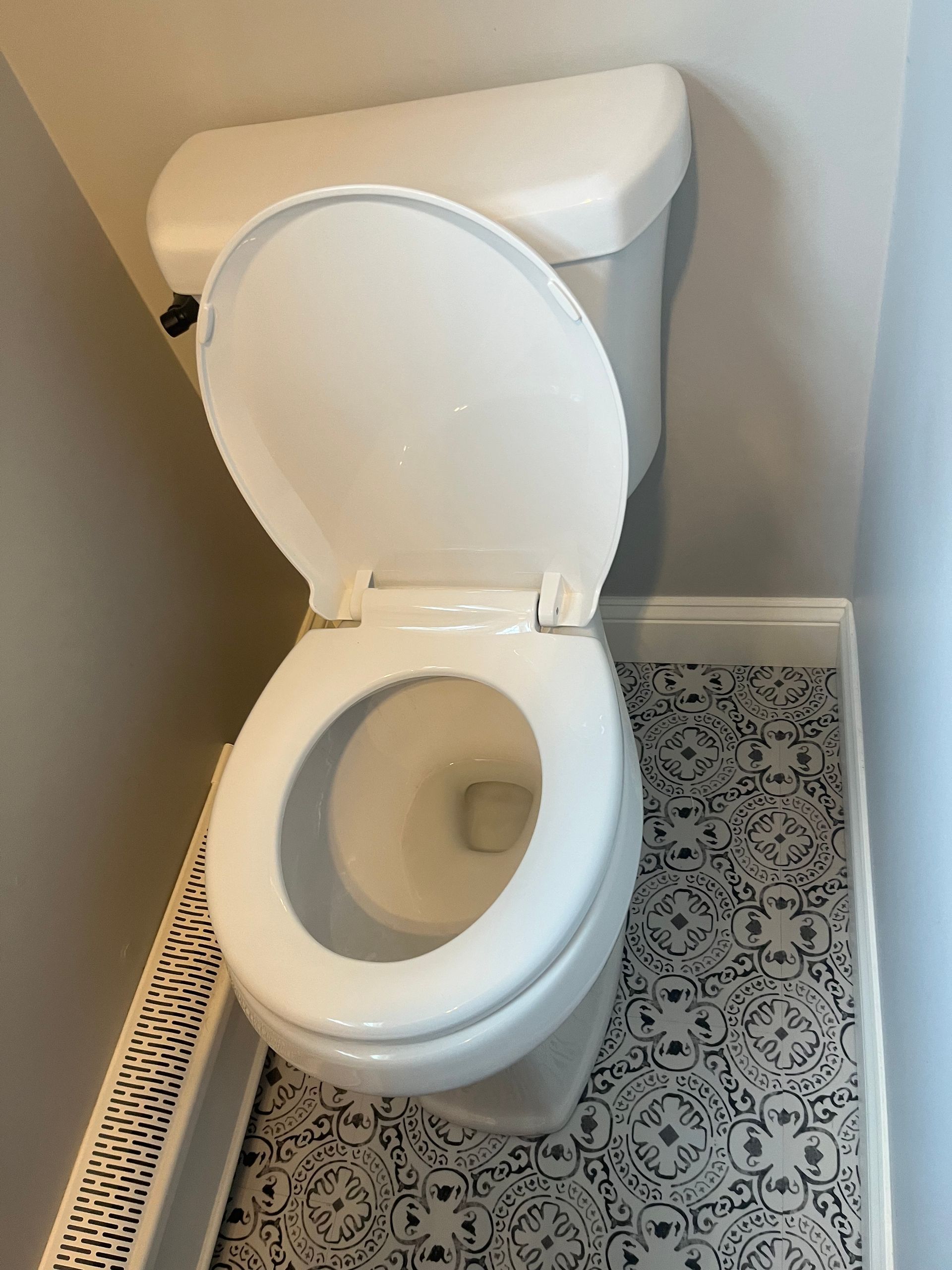 White toilet with lid up in a small bathroom with patterned black-and-white floor tile.