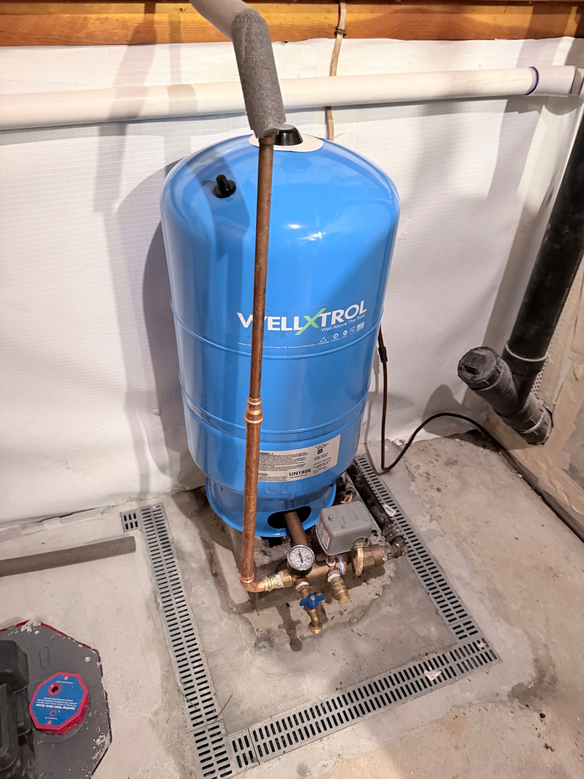 Blue boiler/water heater in a utility room, with copper piping and a floor drain nearby