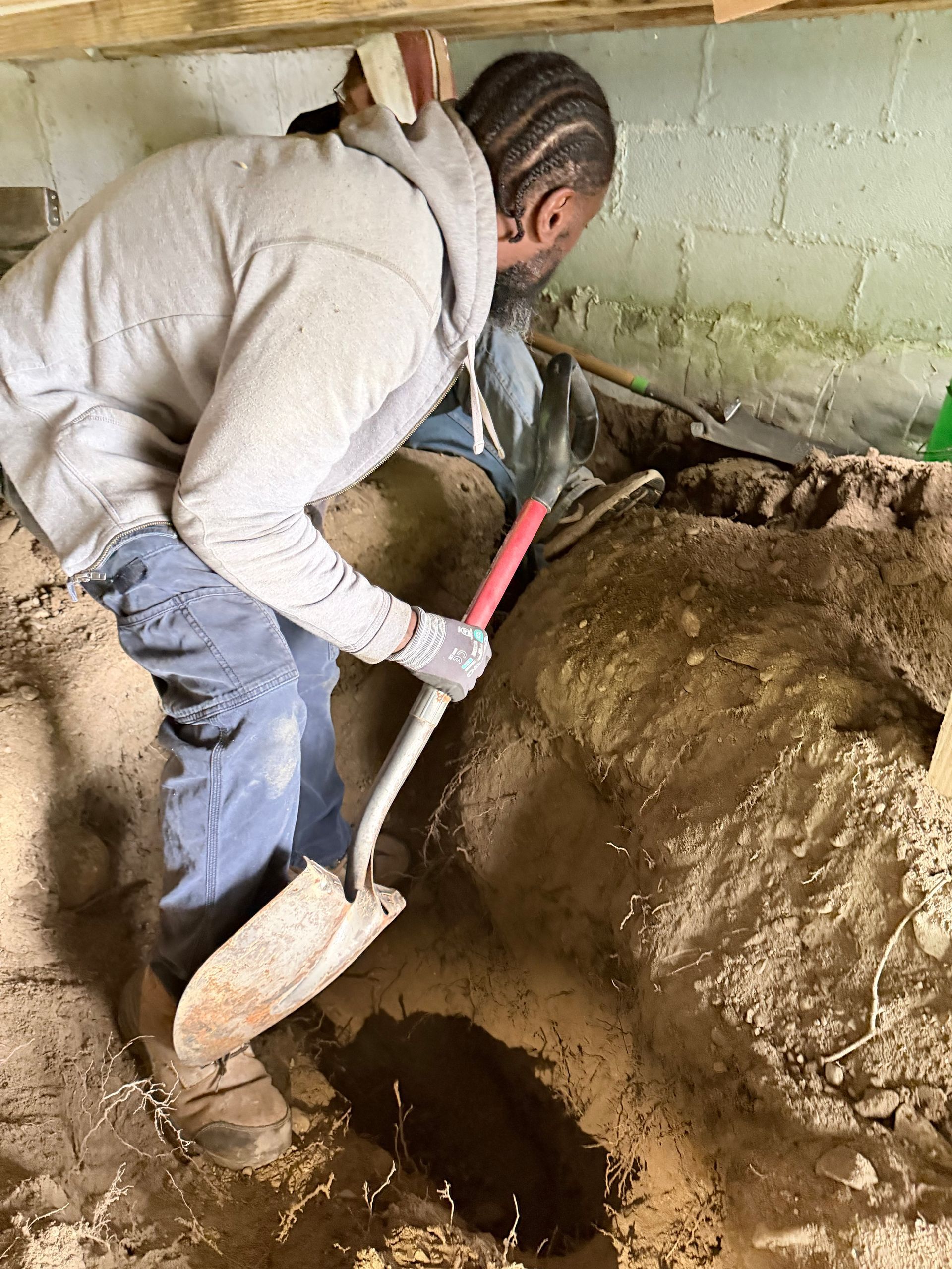 Person digging a large hole with a shovel in a dirt-filled interior space