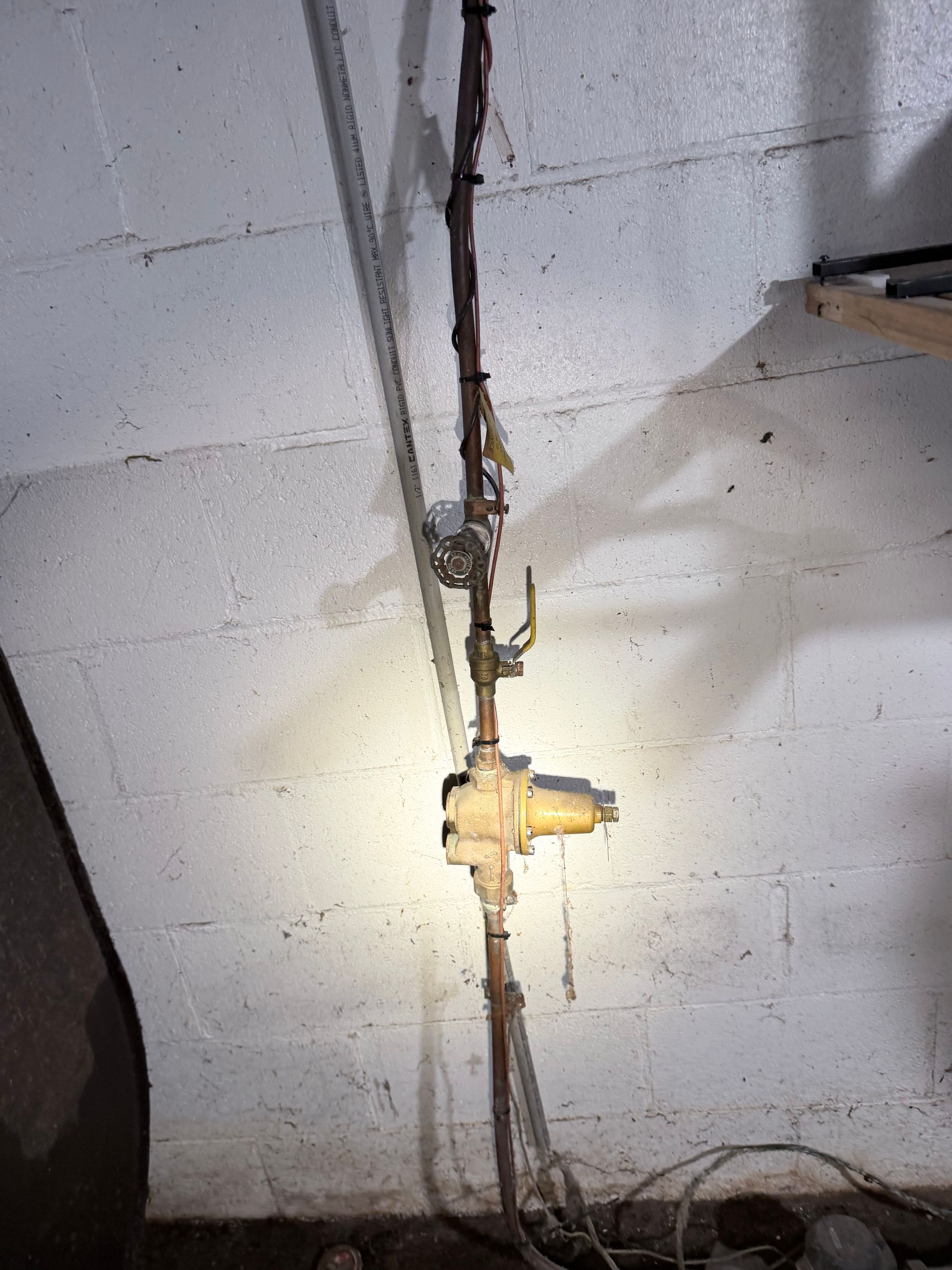 Basement wall with exposed electrical conduit and a junction box against cinder blocks, lit by a flashlight.