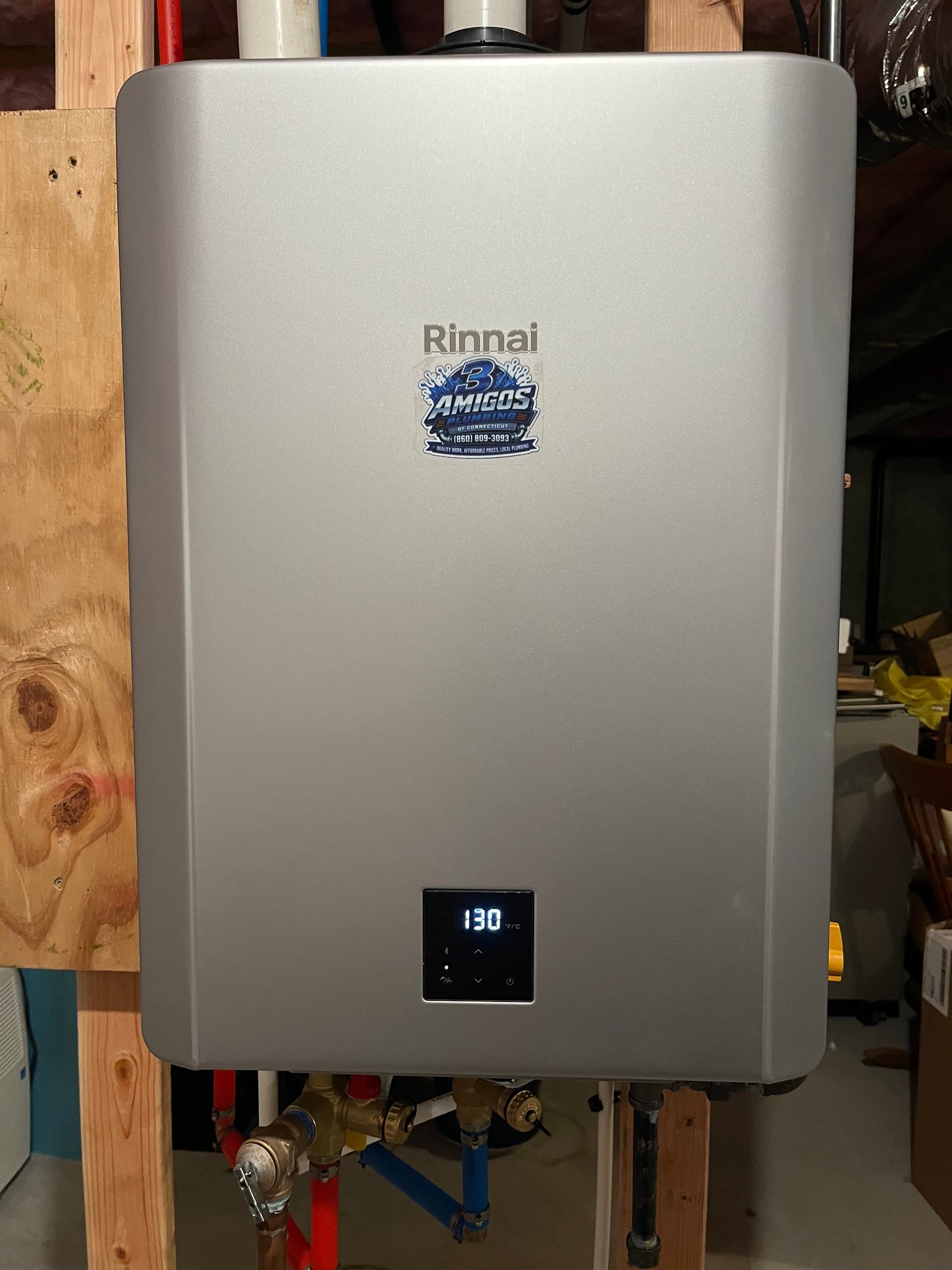 Rinnai tankless water heater mounted on a wooden wall in a utility area, with a small digital display.