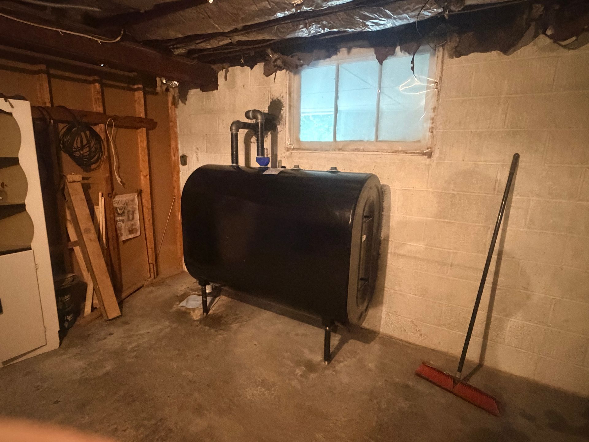 Basement utility room with a black oil tank, concrete floor, and a red broom leaning against a wall.