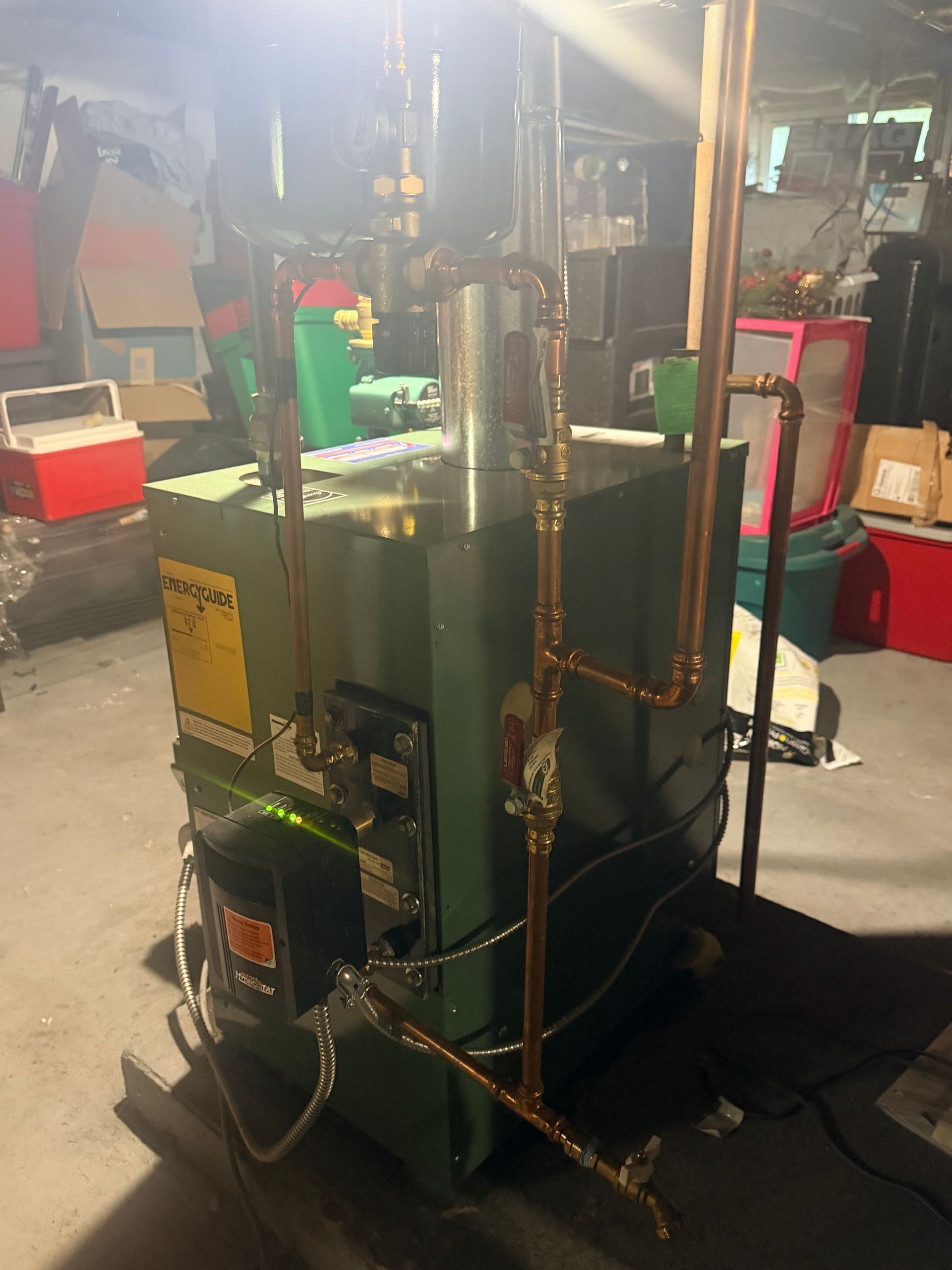 Large green industrial machine with copper pipes and a pressure gauge in a workshop.