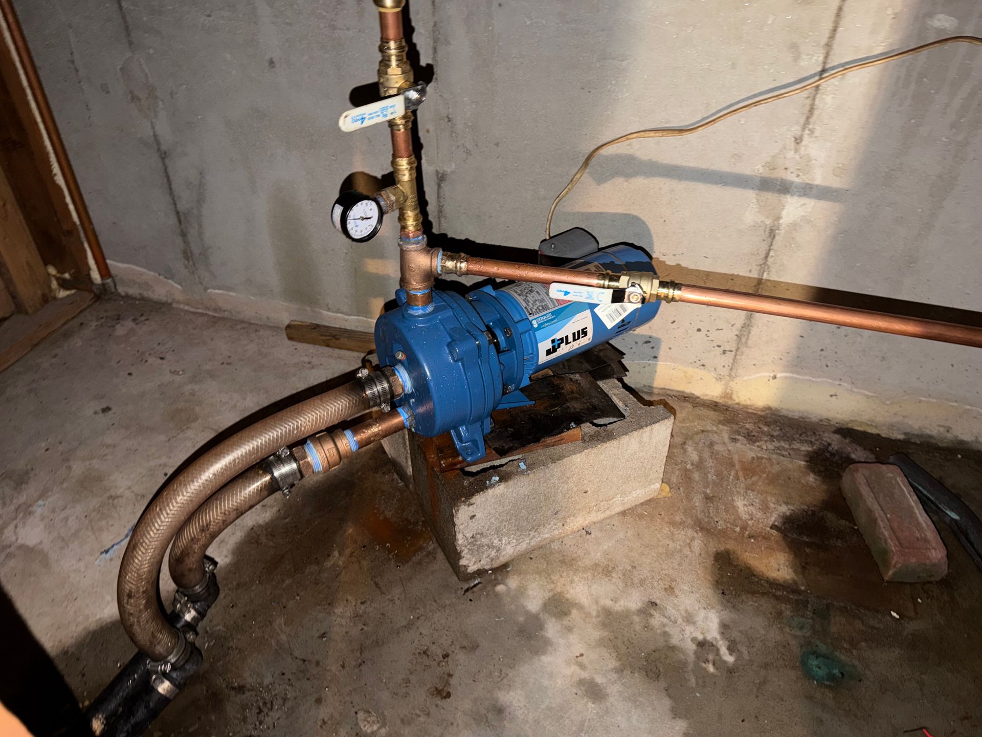 Blue water pump and pipes installed on a concrete floor in a utility room.