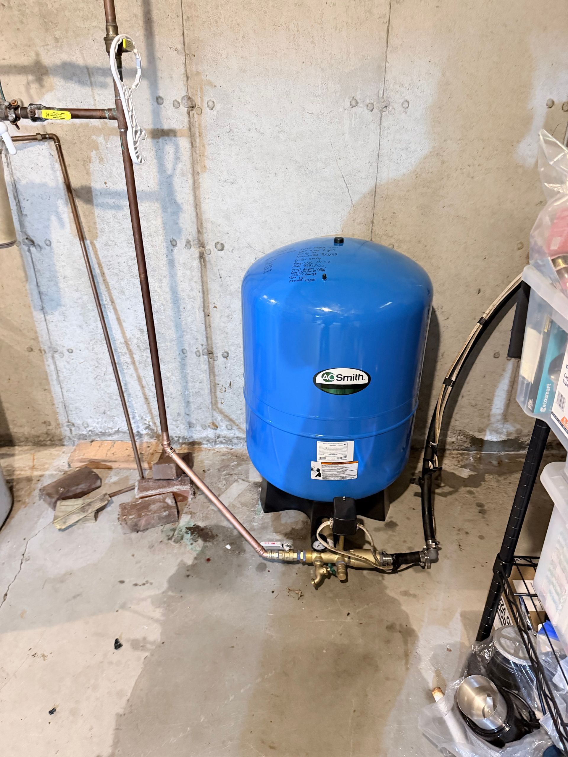 Blue water heater tank in unfinished basement with exposed pipes and concrete floor