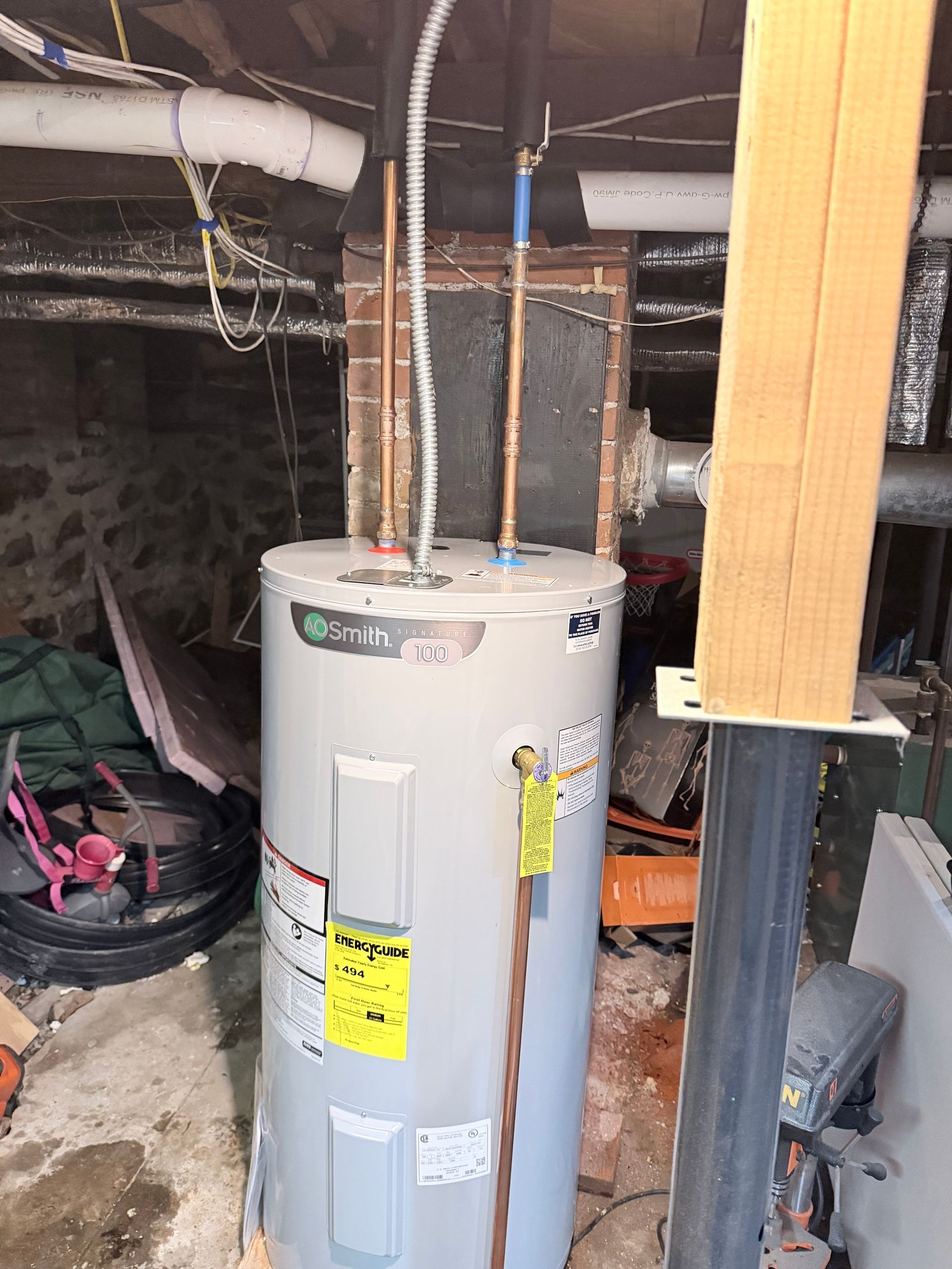 Water heater in a basement with exposed pipes and utility equipment.