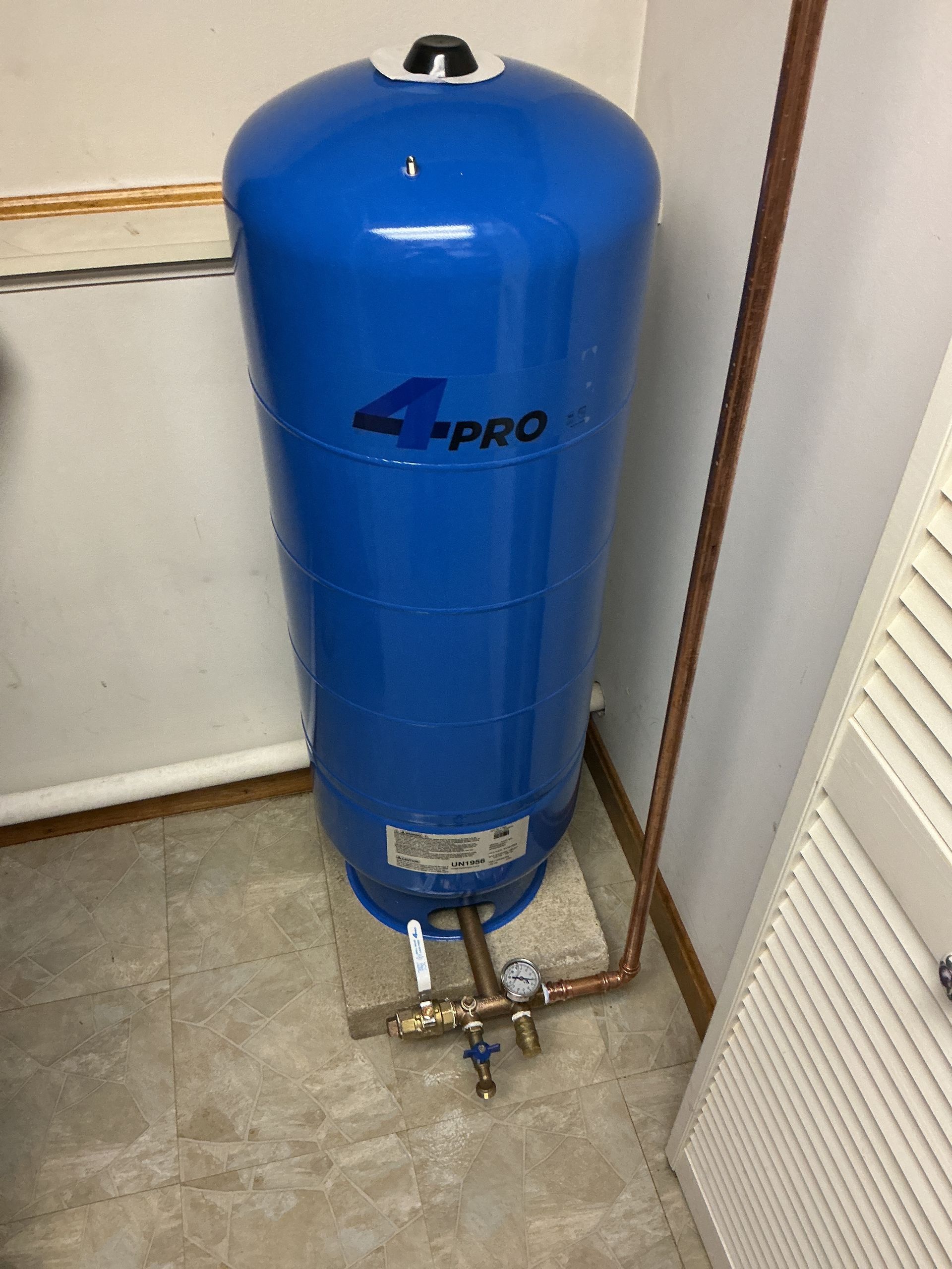 Blue upright water pressure tank with pipes and valves in a utility room corner