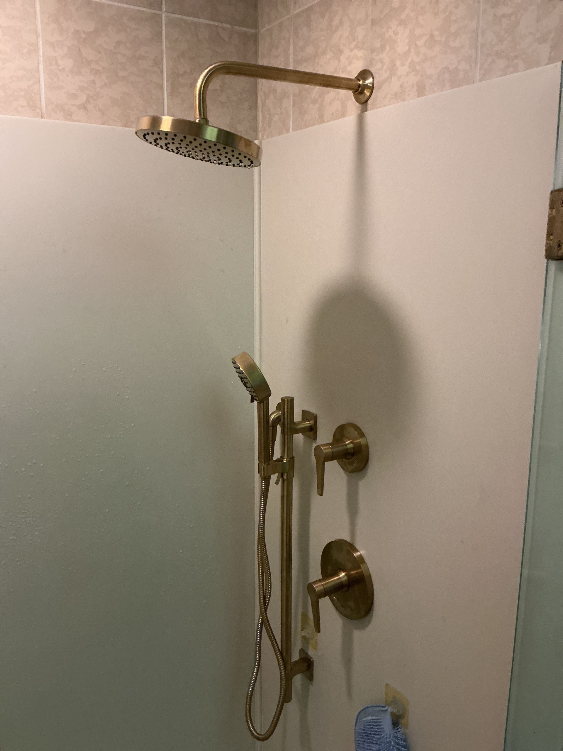 Shower stall with gold fixtures, handheld showerhead, and frosted glass doors
