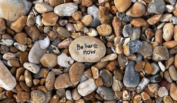 A pile of rocks with a small rock that says be here now on it.