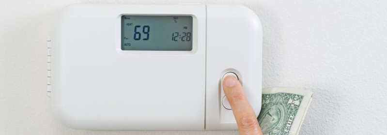 A hand pressing a thermostat button. A dollar bill is partially visible beneath.