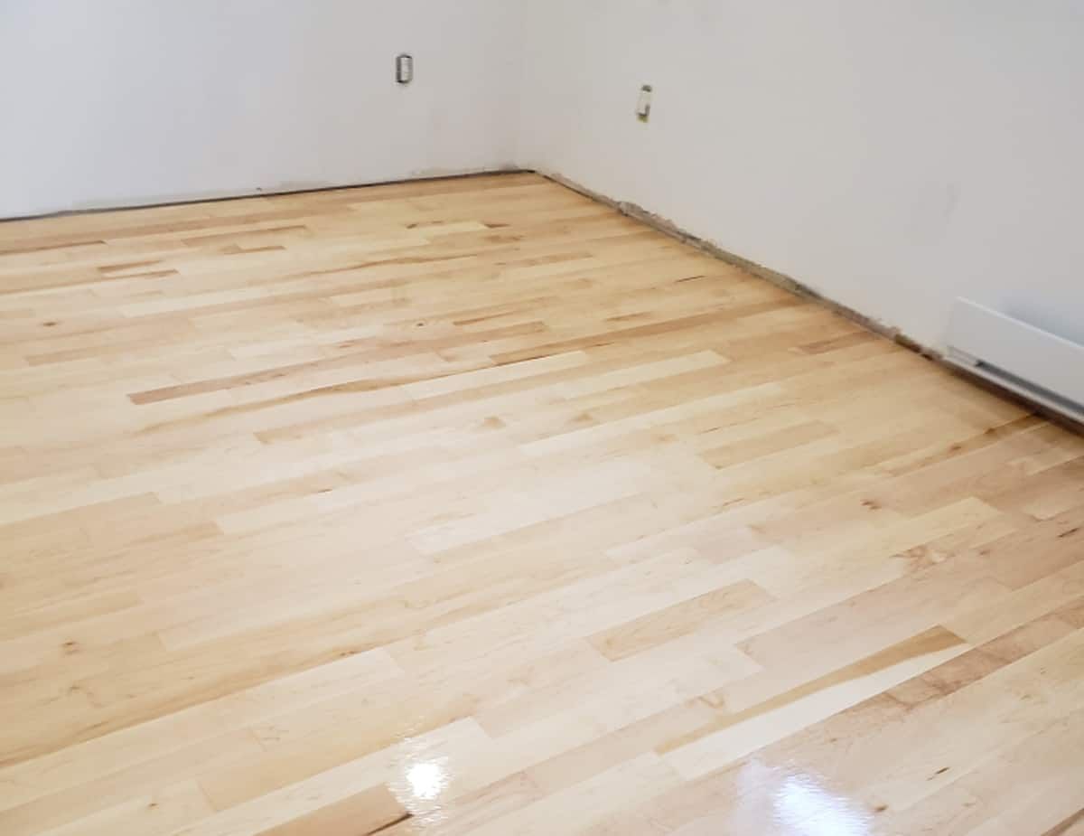 Plancher de bois clair dans une pièce vide avec des murs blancs et un radiateur à plinthe.