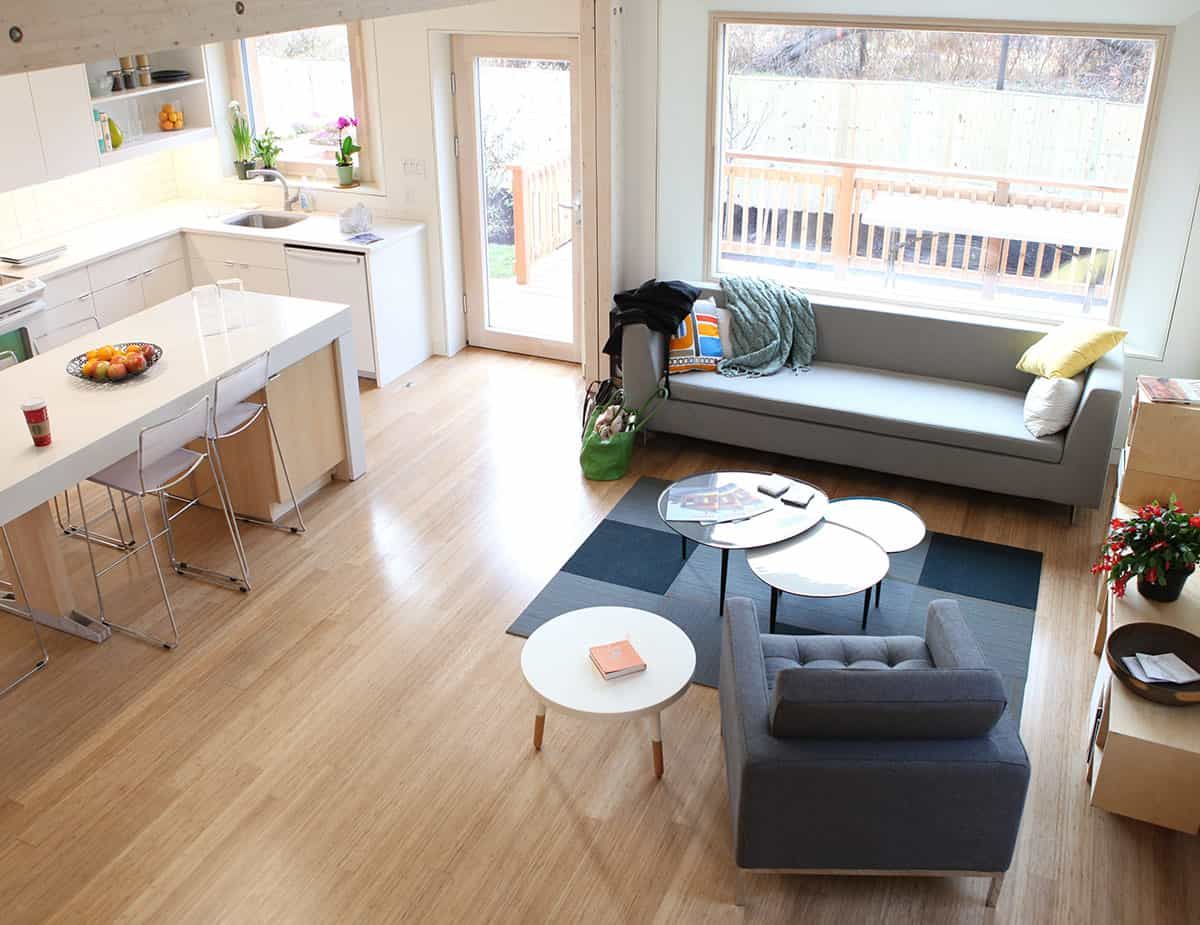 Salon moderne avec parquet, canapé gris et cuisine blanche.
